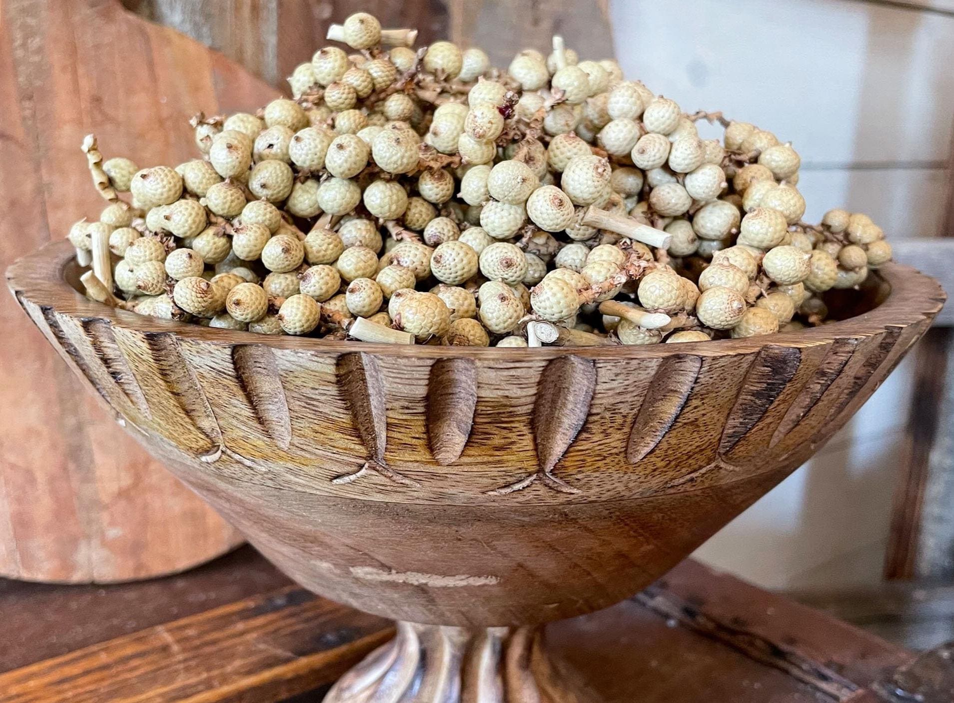 Wooden bowl filled with white botanical canella berries on a wooden surface.