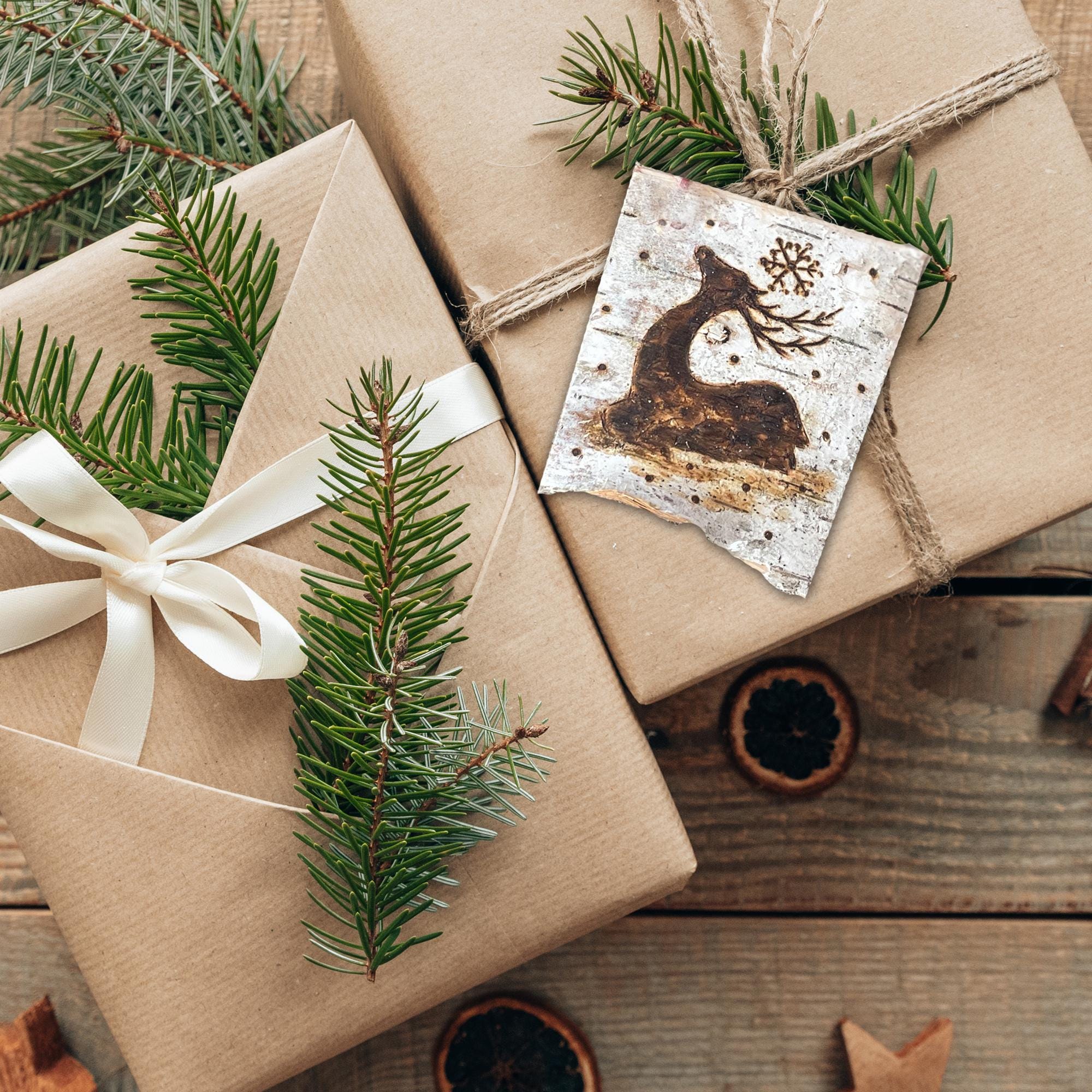 Gifts wrapped in brown paper with greenery and a card featuring a deer on a wooden surface.