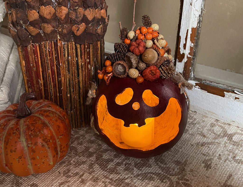 Decorative pumpkin with a carved face, surrounded by pinecones and other fall elements on a textured surface.