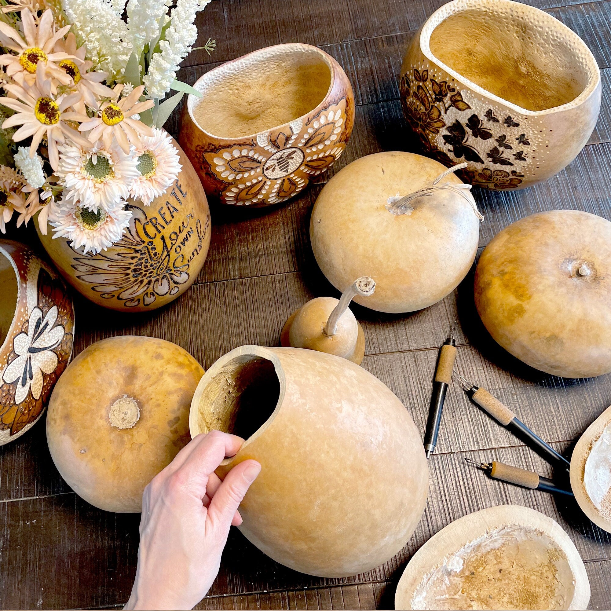 Decorative gourds on a wooden surface with a hand interacting with one of the gourds.