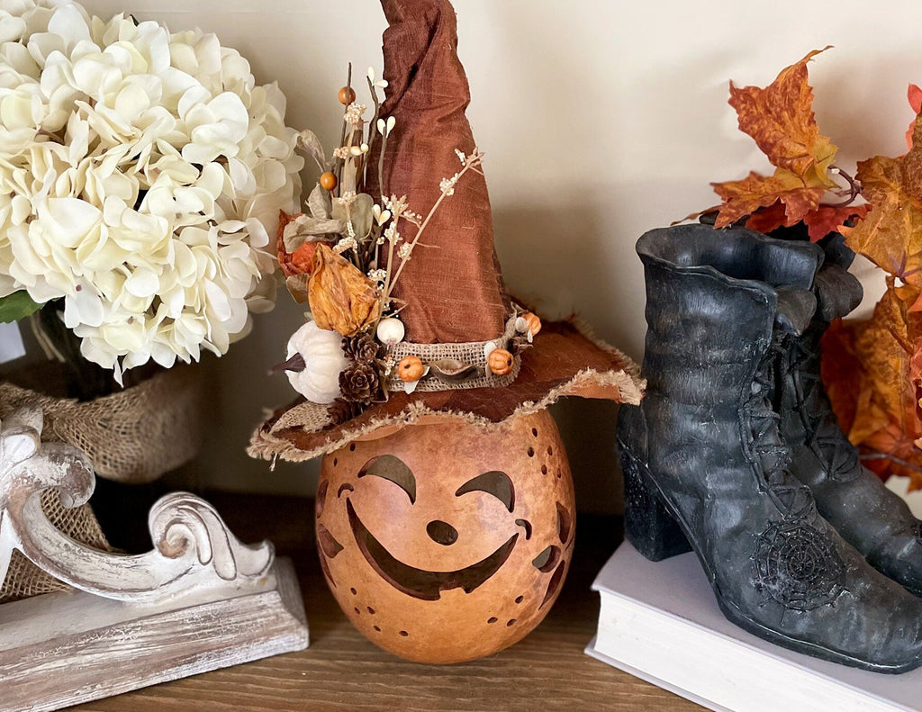 Decorative items including a pumpkin lantern, witch hat, and boots on a shelf with flowers and leaves.
