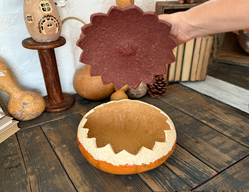 Decorative gourd with lid on a wooden surface, surrounded by pumpkins and a small house ornament.