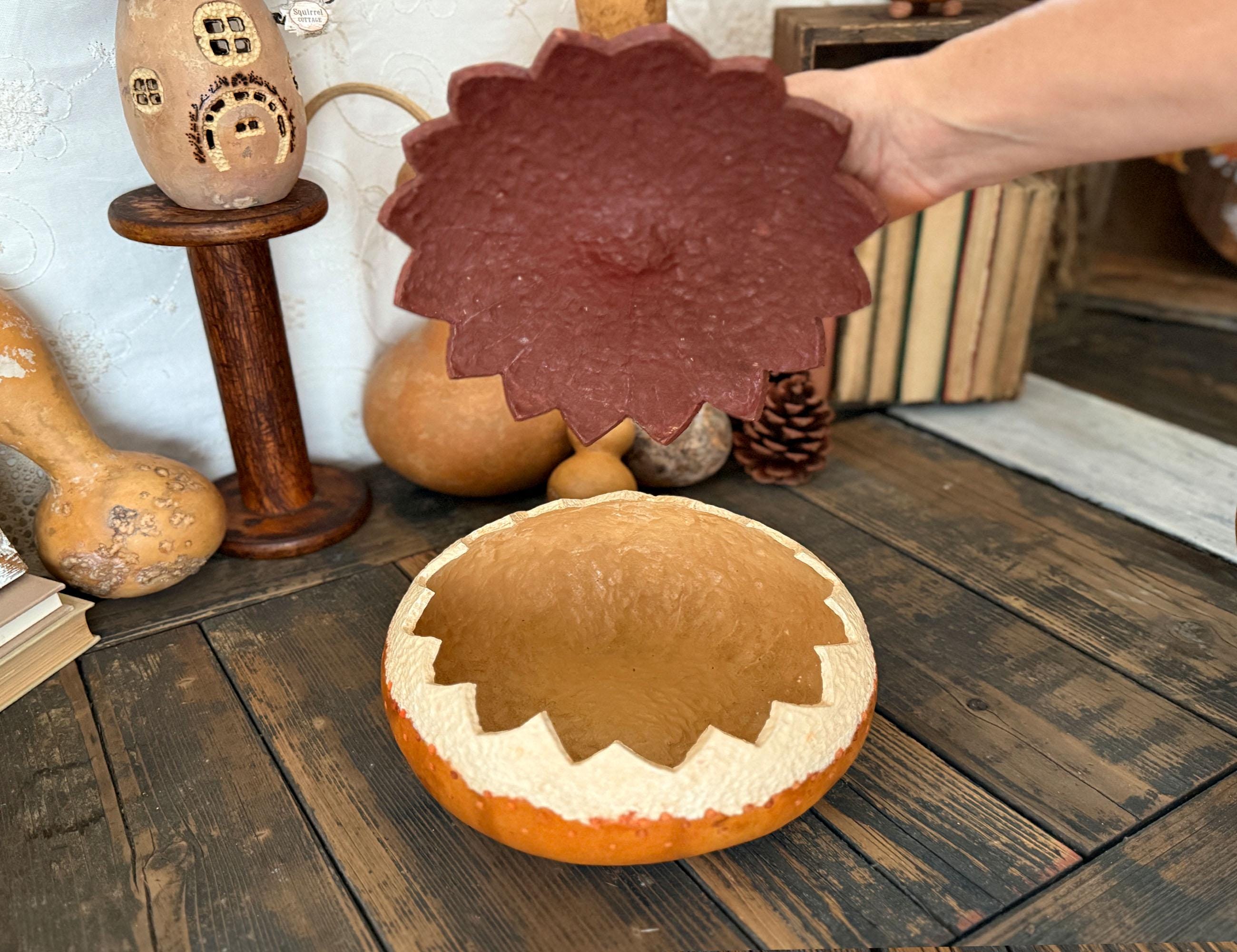 Decorative gourd with lid on a wooden surface, surrounded by pumpkins and a small house ornament.
