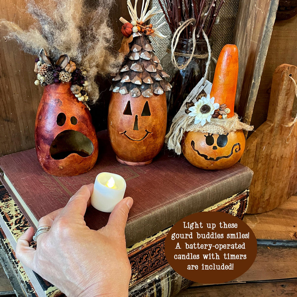 Decorative gourds with faces on a rustic surface, one being lit by a hand.