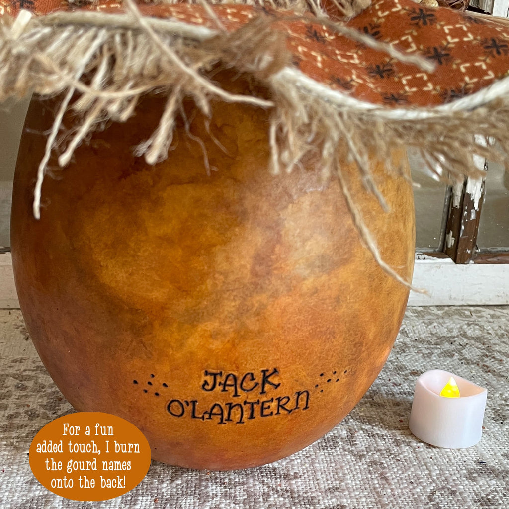 Decorative gourd labeled 'Jack O'Lantern' with twine and a small candle on a textured surface.