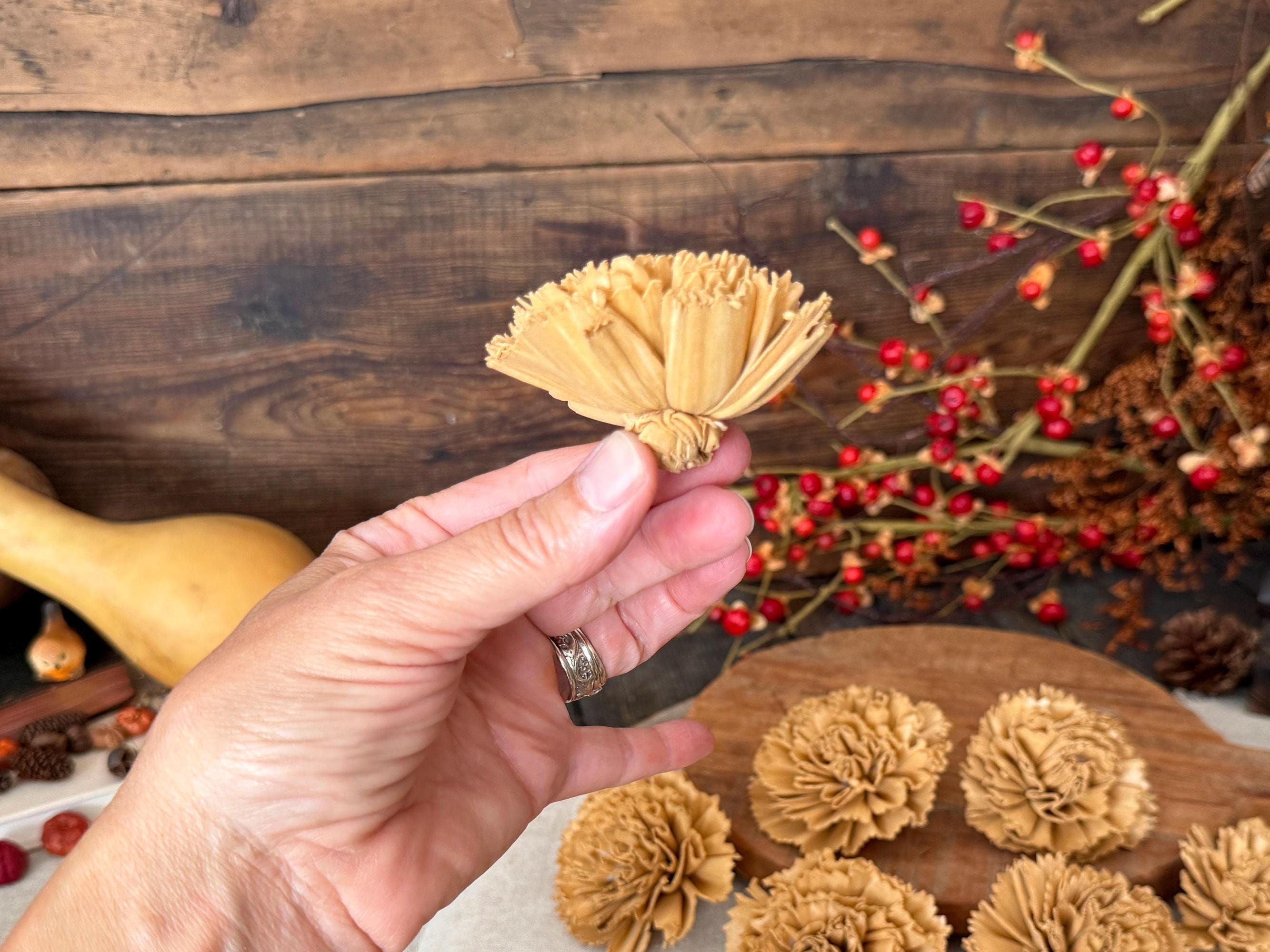 Hand holding a wood flower blossom in profile with a wooden background and red berries