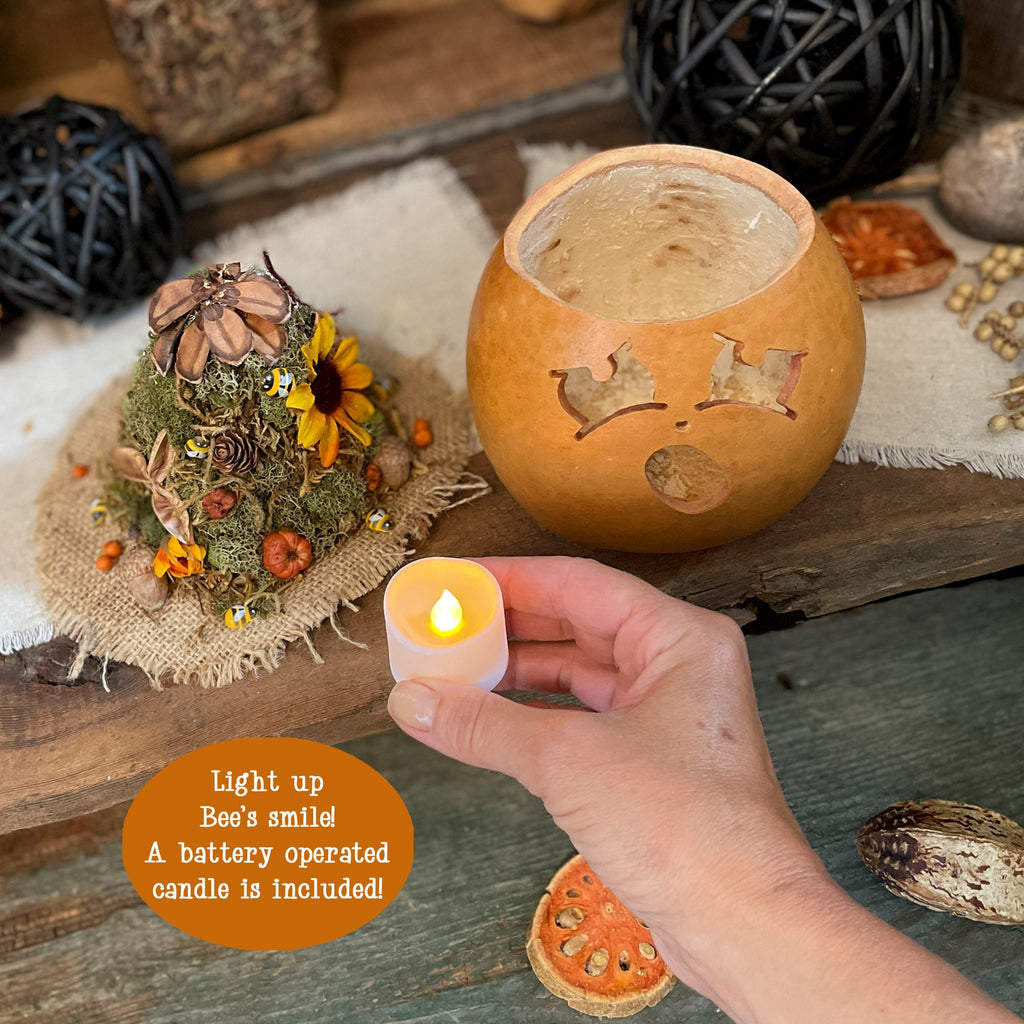 Hand holding a lit candle next to a carved pumpkin with decorative elements on a wooden surface.