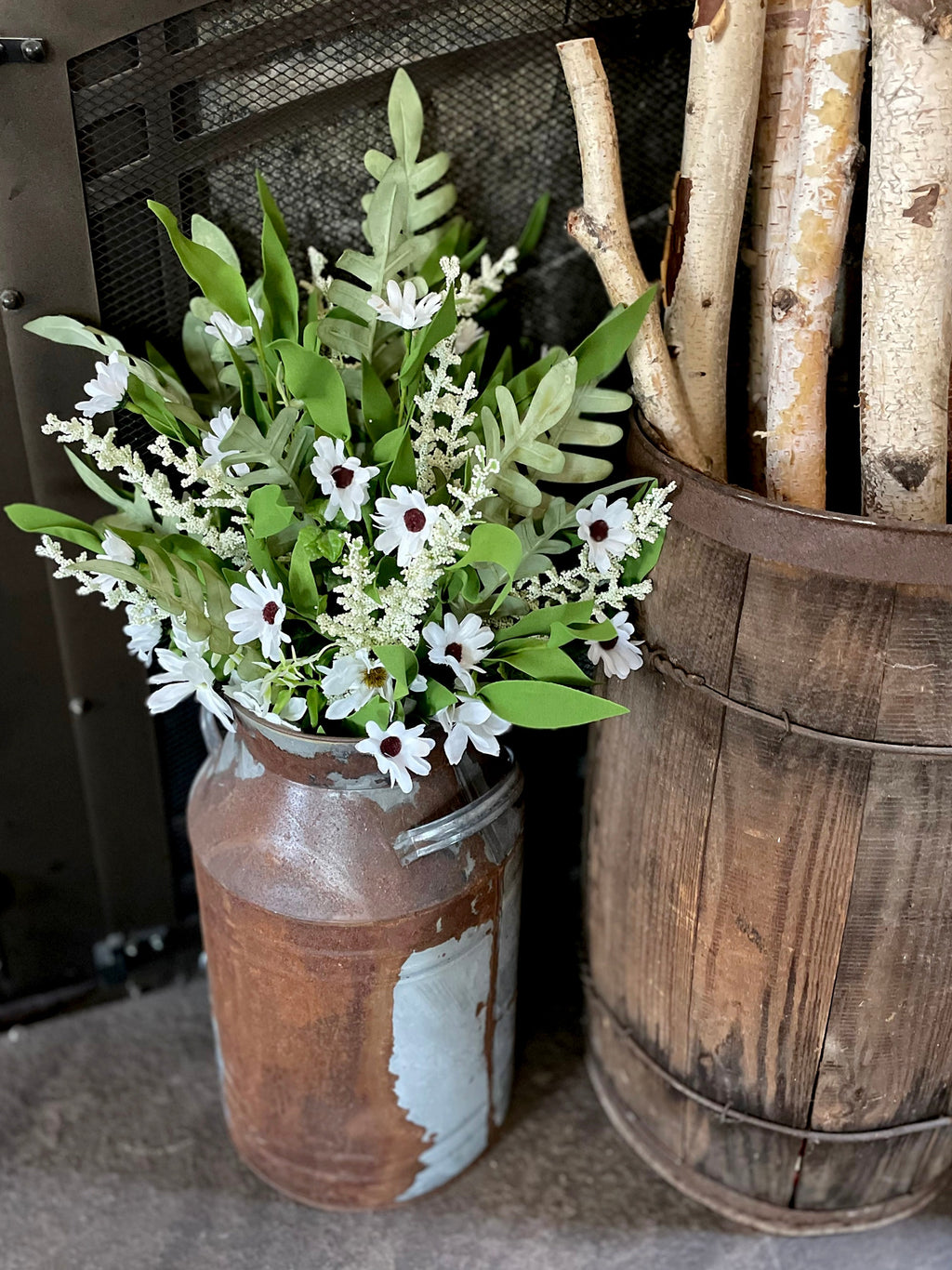 Decorative arrangement of flowers in a rustic metal container next to a wooden barrel with firewood.