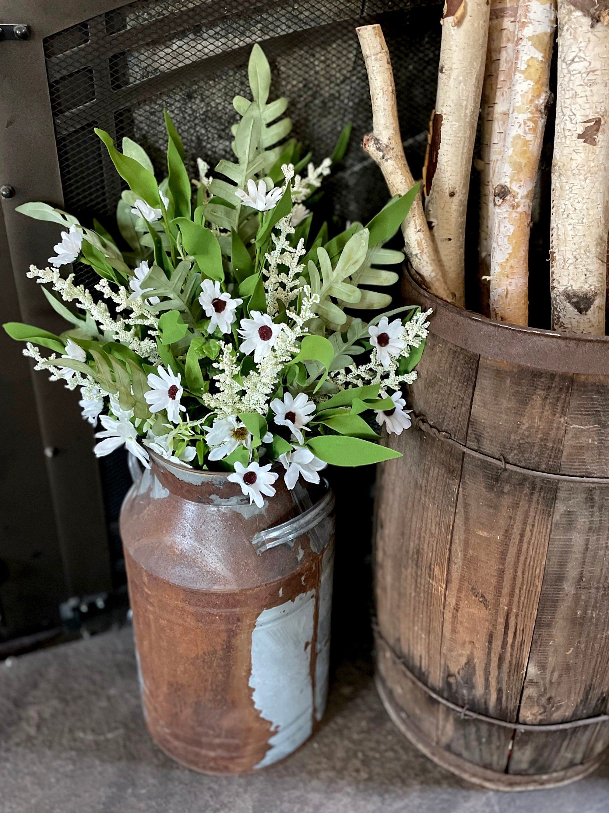 Decorative arrangement of flowers in a rustic metal container next to a wooden barrel with firewood.