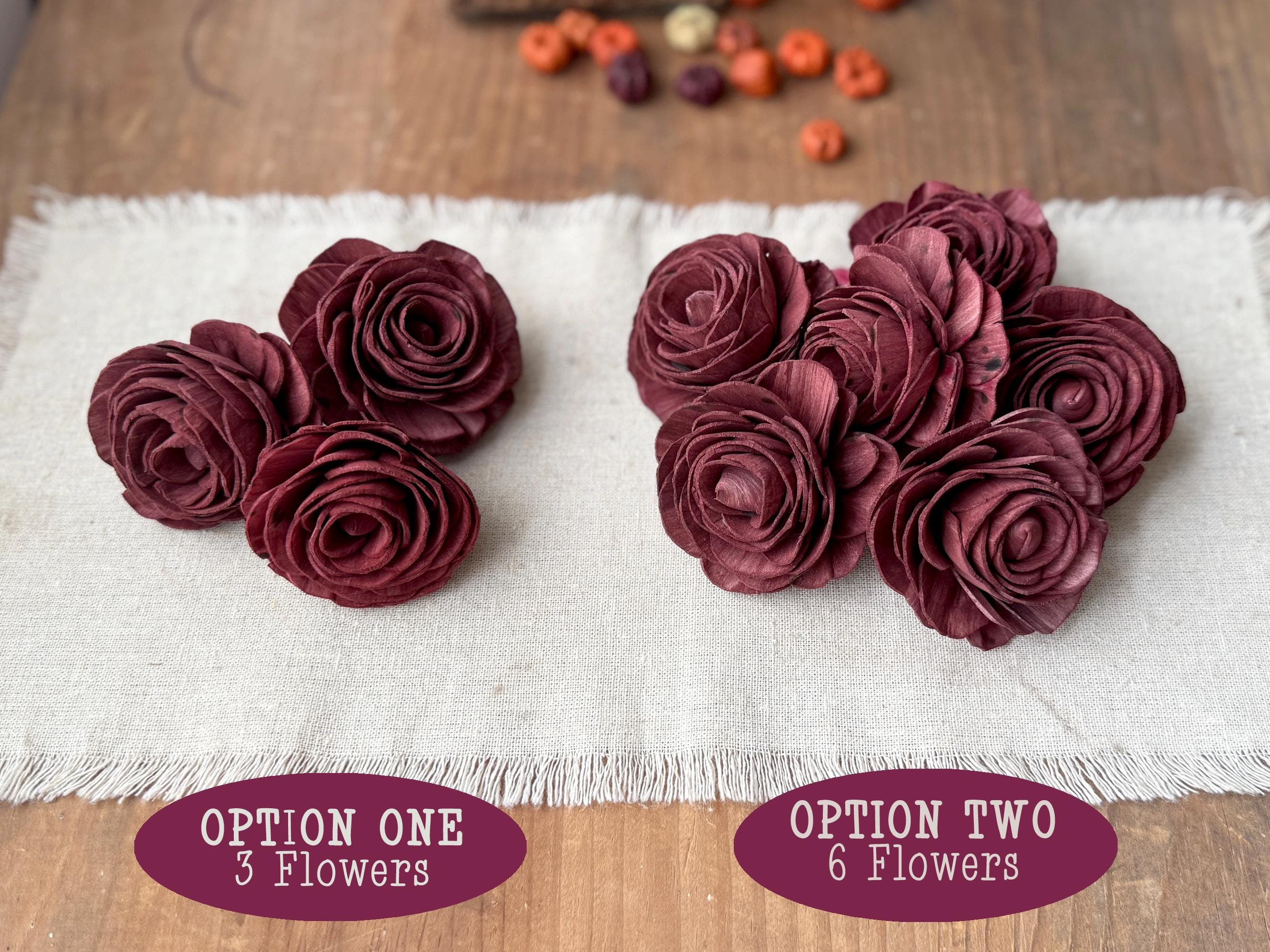 Two sets of maroon wood flower arrangements labeled 'Option One' with 3 flowers and 'Option Two' with 6 flowers on a white cloth.
