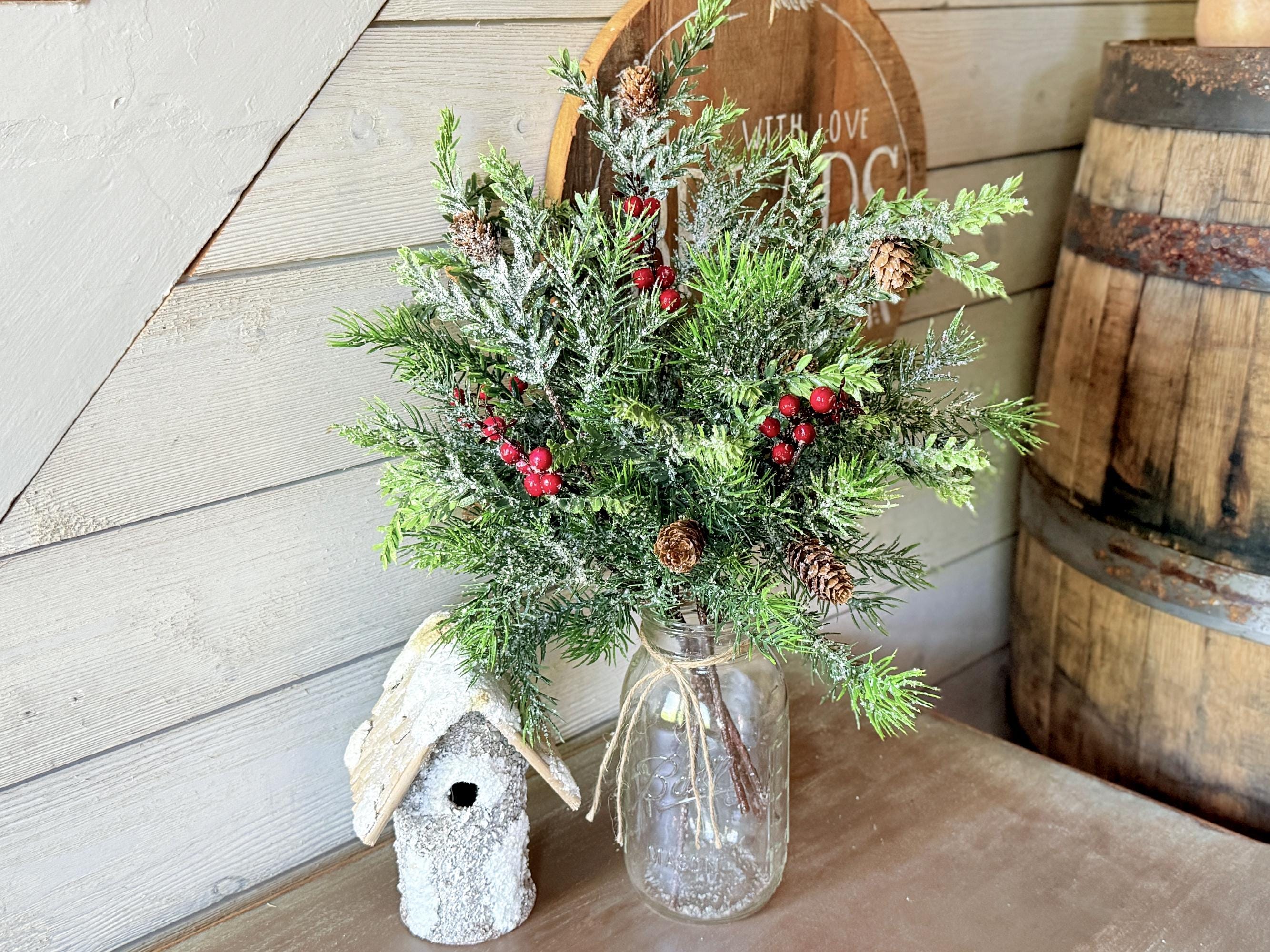 Bouquet of greenery with red berries in a glass vase on a wooden surface, with a rustic background.
