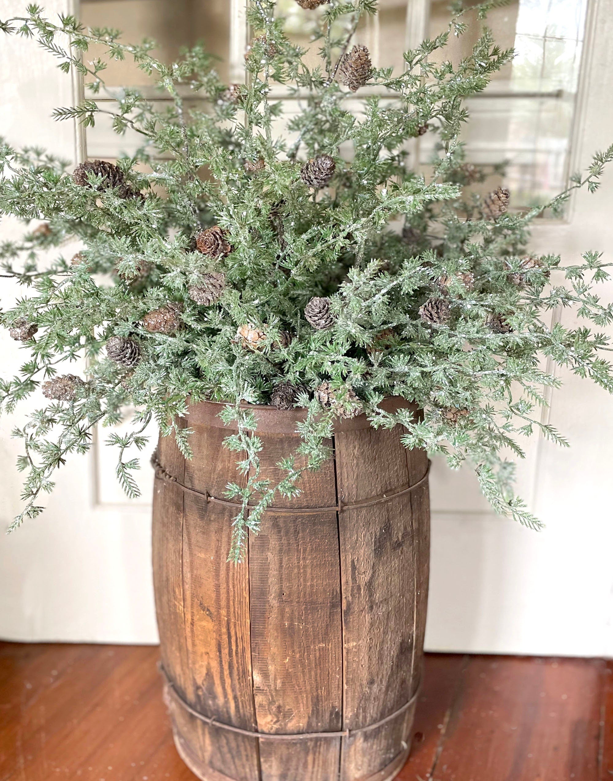 Decorative nail bucket with iced greenery and pinecones on a wooden floor.