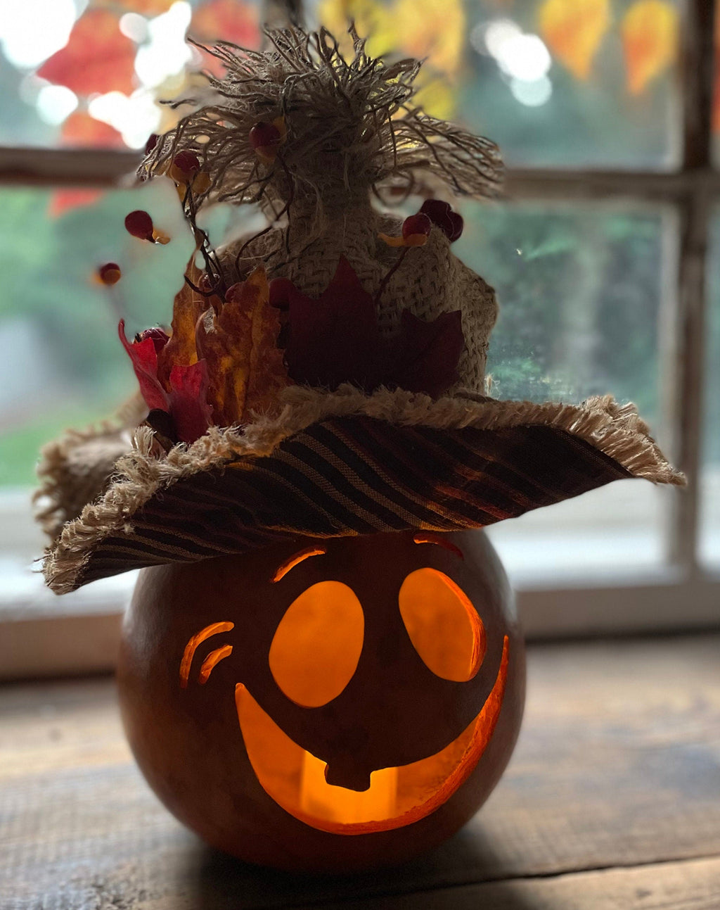 Decorative pumpkin with a face and straw hat on a wooden surface, with a blurred background.
