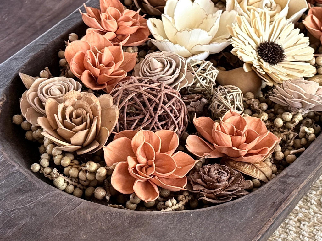 Decorative floral arrangement in a large wooden dough bowl on a coffee table. Flowers are orange and beige