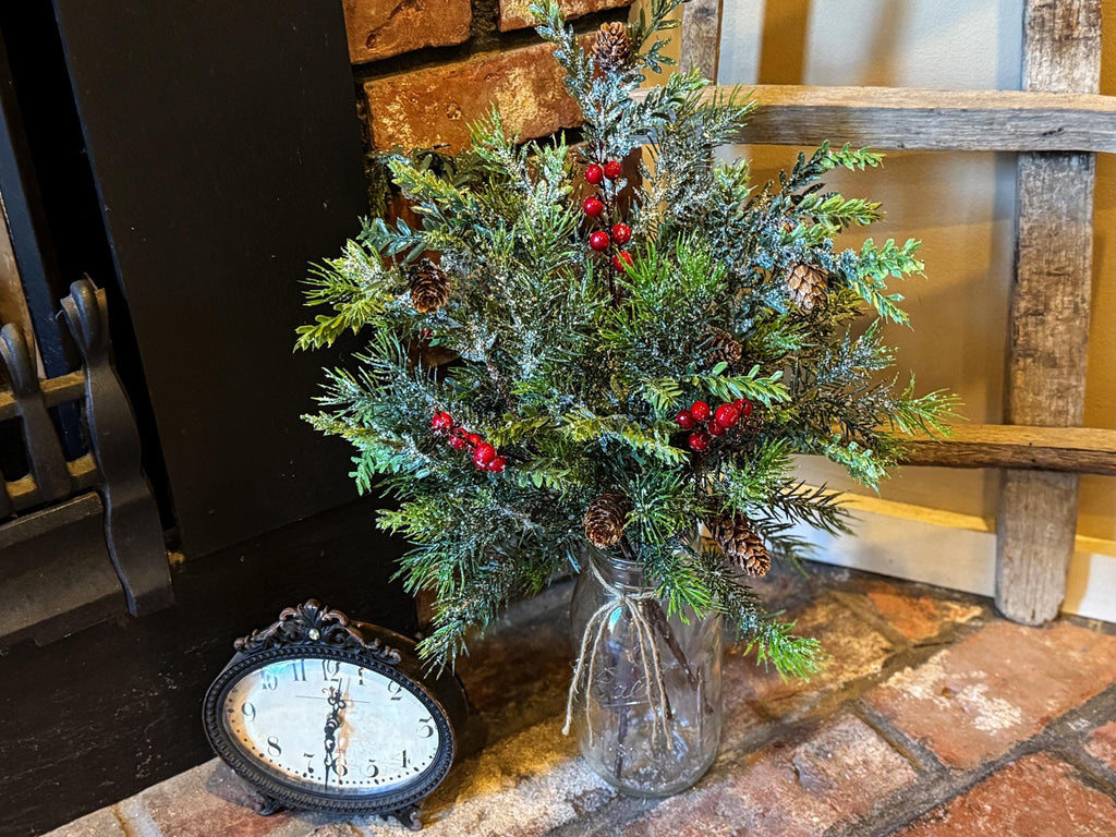 Decorative Christmas arrangement in a glass vase on a stone hearth with a clock.