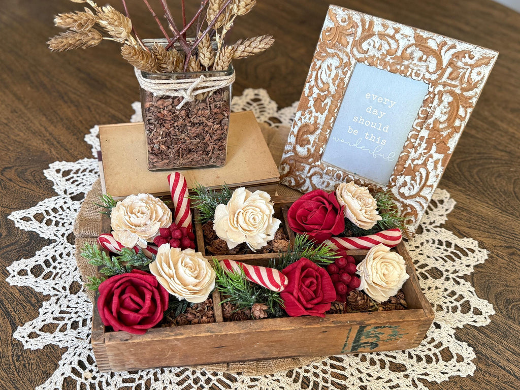 Decorative arrangement with flowers, candy canes, and a photo frame on a lace tablecloth.