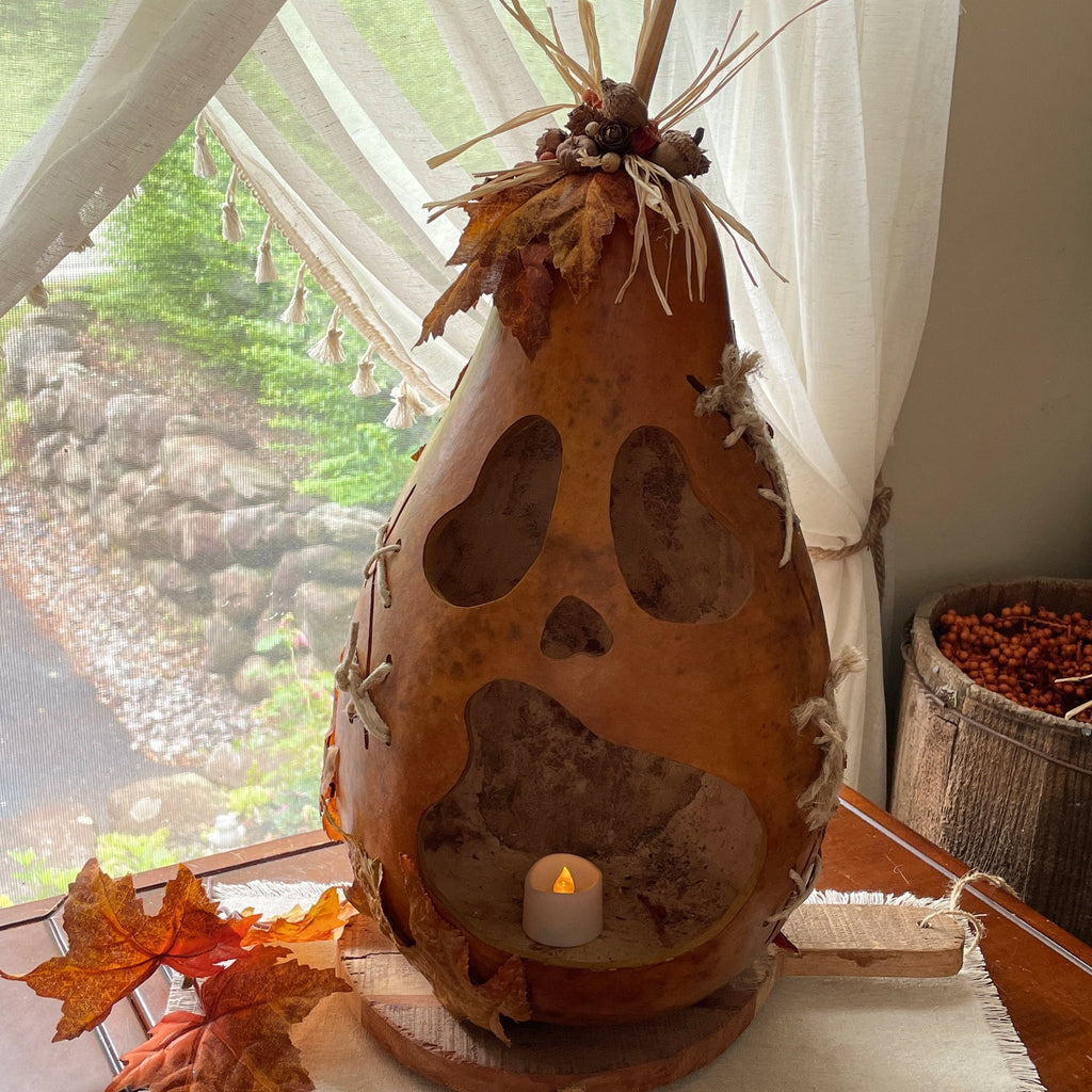 Decorative gourd with a candle inside, surrounded by autumn leaves and a scenic window view.