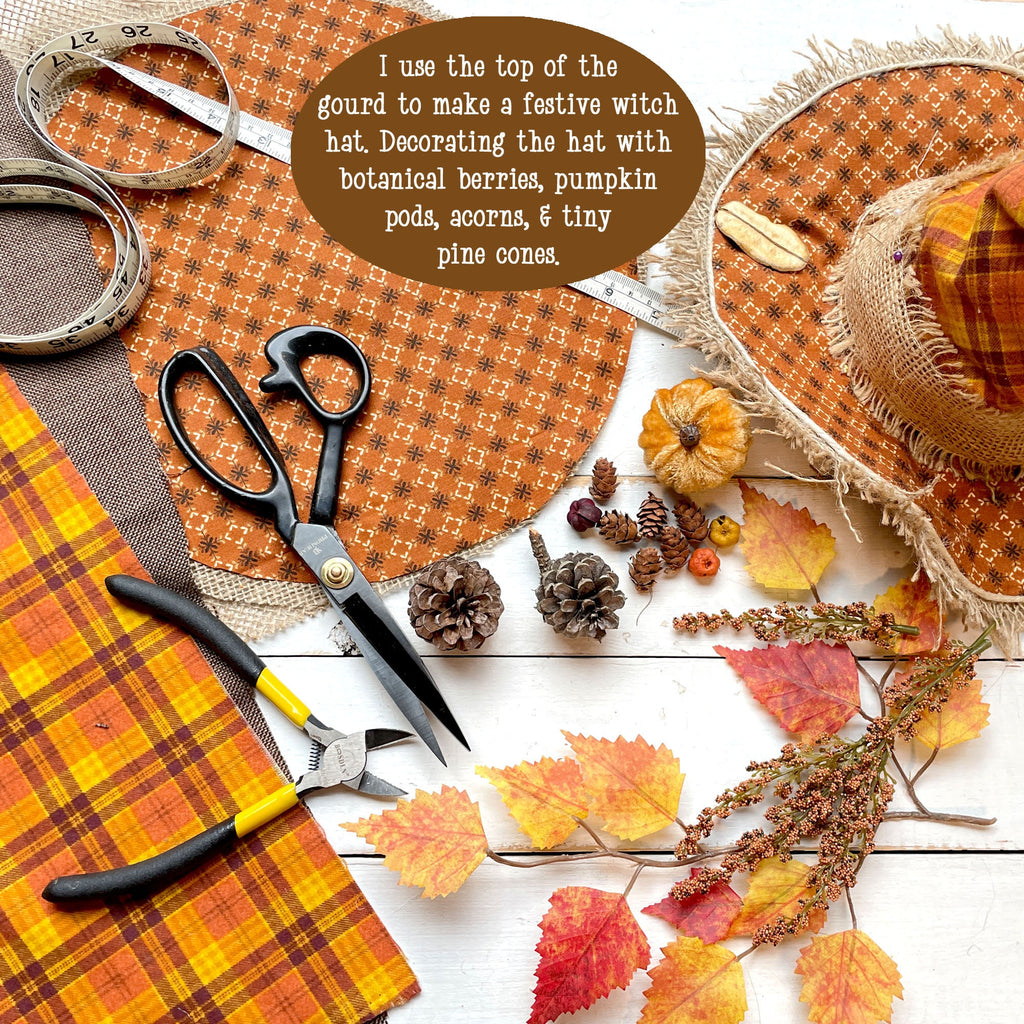 Decorative witch hat with autumn elements on a table with scissors and fabric.