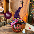 Decorative Halloween pumpkin with a witch hat on a wooden surface, surrounded by festive decorations.