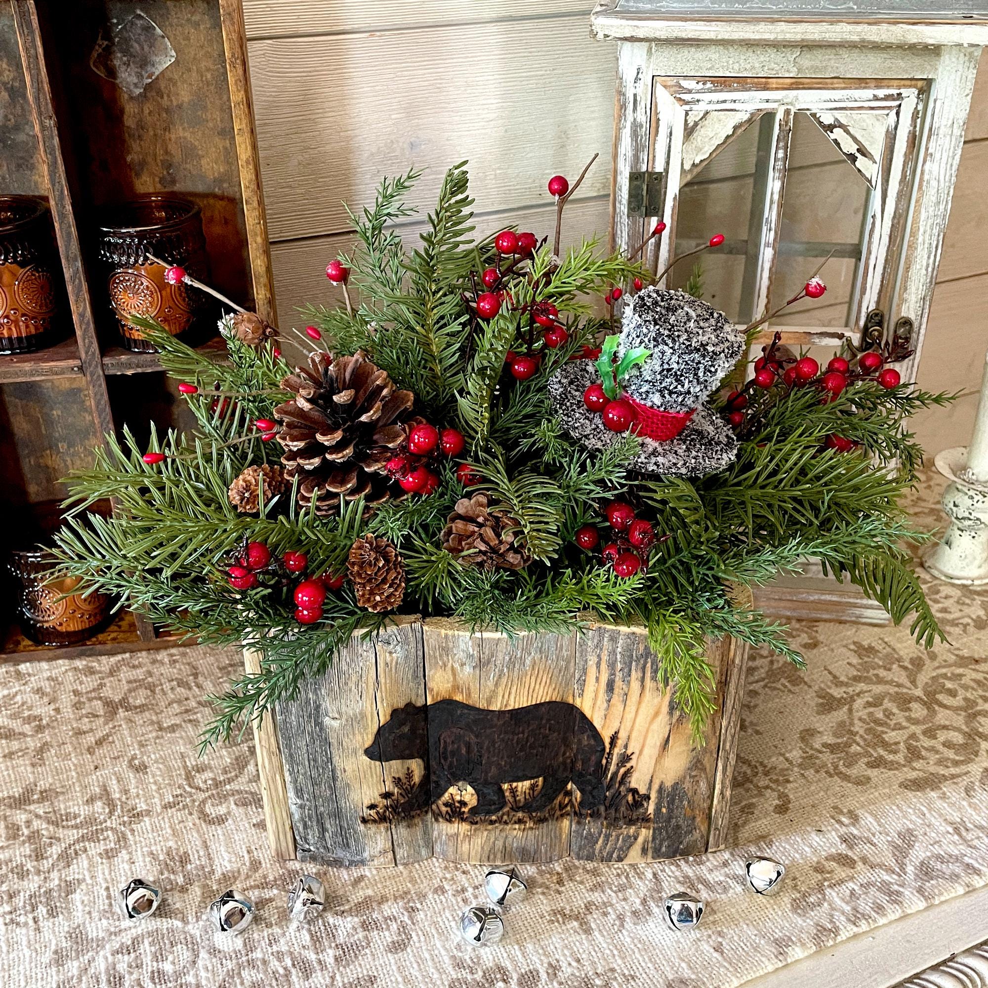 Decorative Christmas arrangement with pinecones, berries, and a wooden box with a bear silhouette on a rustic surface.