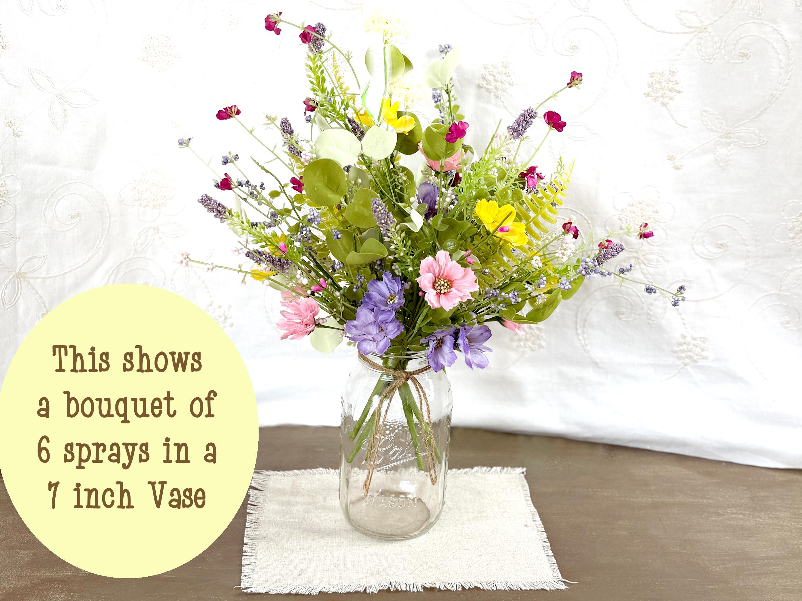 Bouquet of flowers in a clear vase on a wooden surface with a white cloth background
