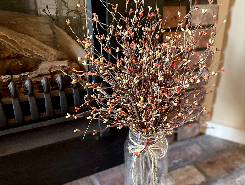 Decorative arrangement of branches with small red berries in a clear glass vase in front of a fireplace.