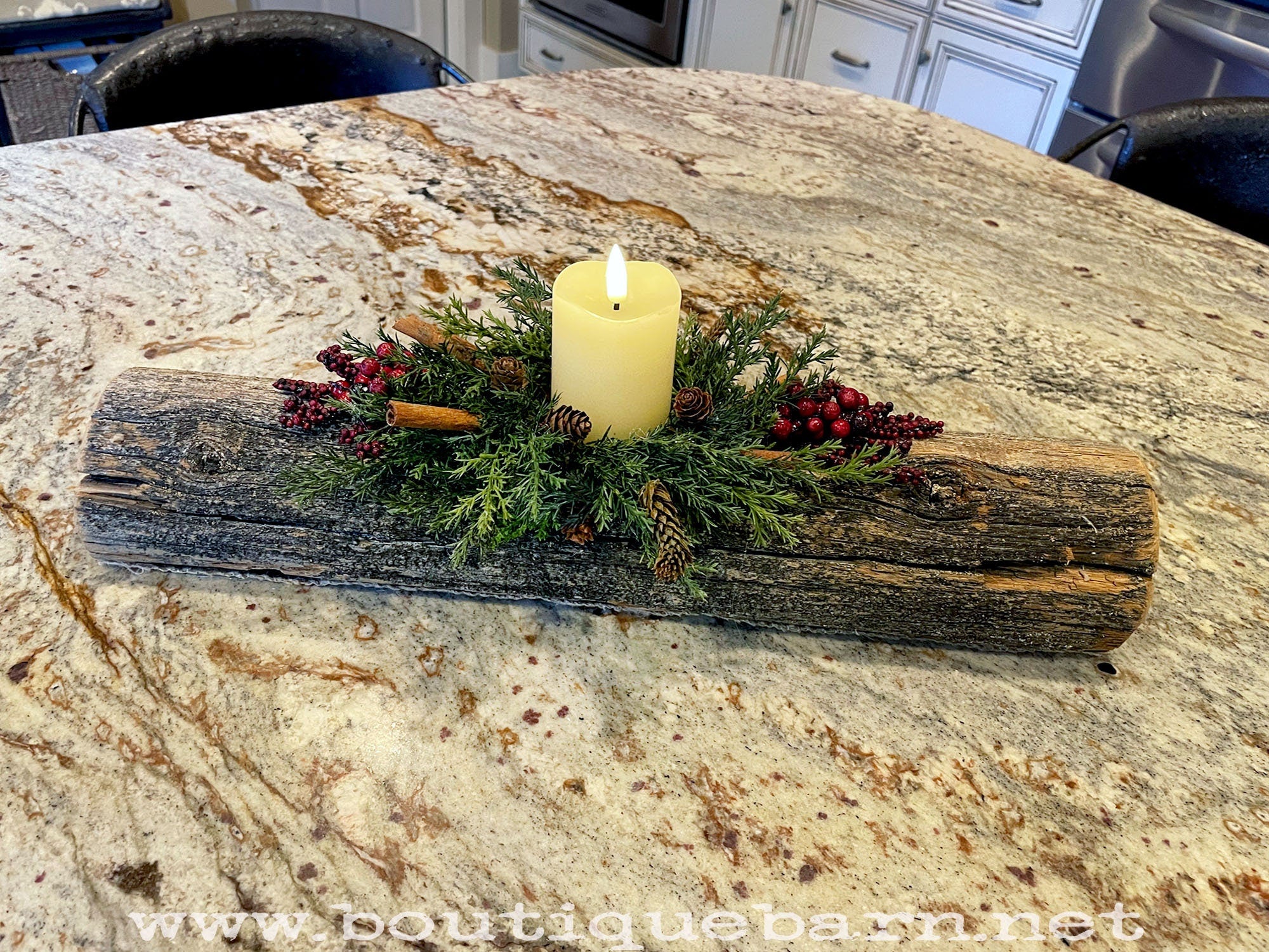 Decorative yule log candle holder with a candle on a marble countertop, featuring greenery and berries.