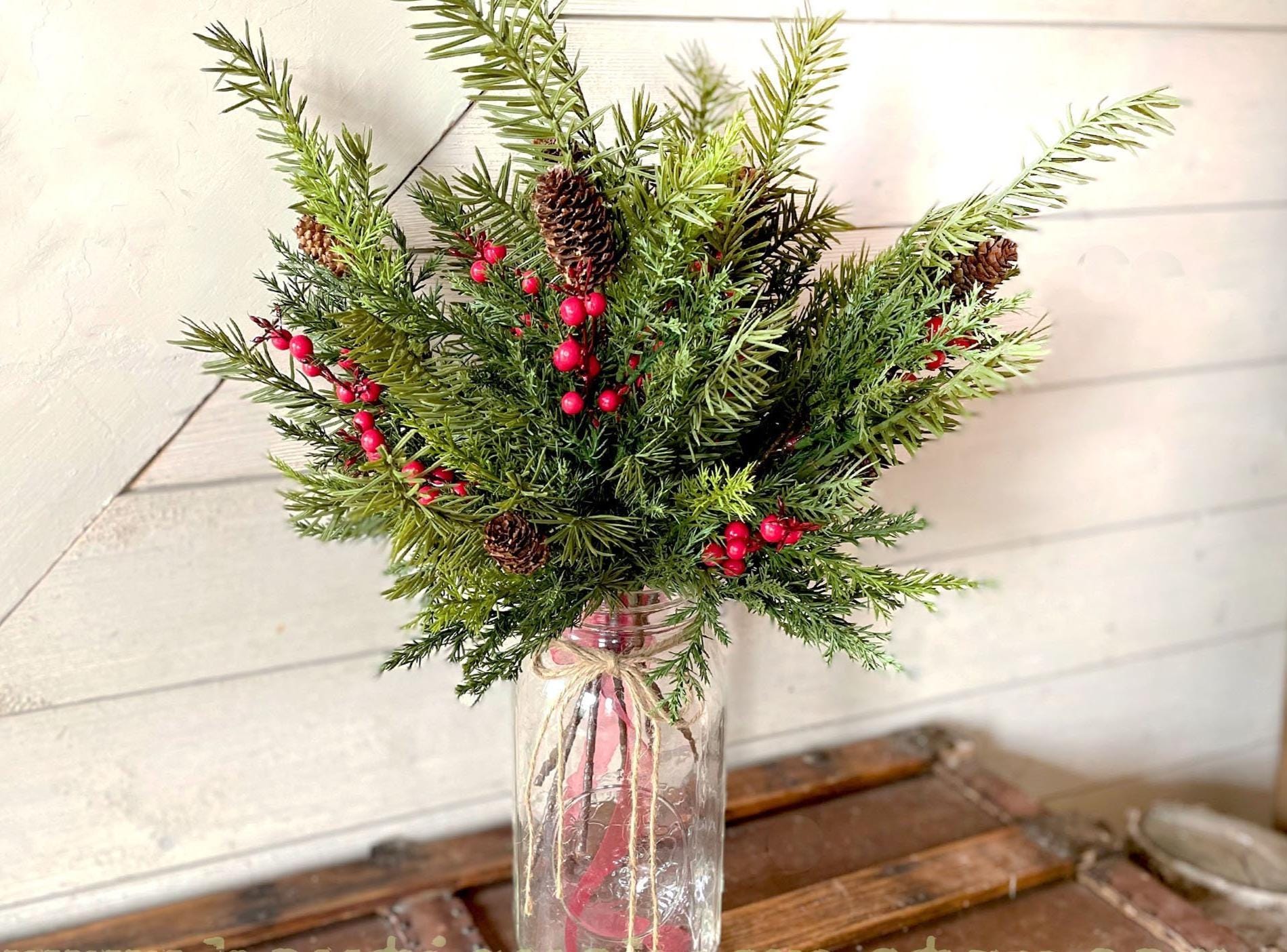 Bouquet of realistic  Christmas greenery with red berries in a clear vase on a wooden surface. 