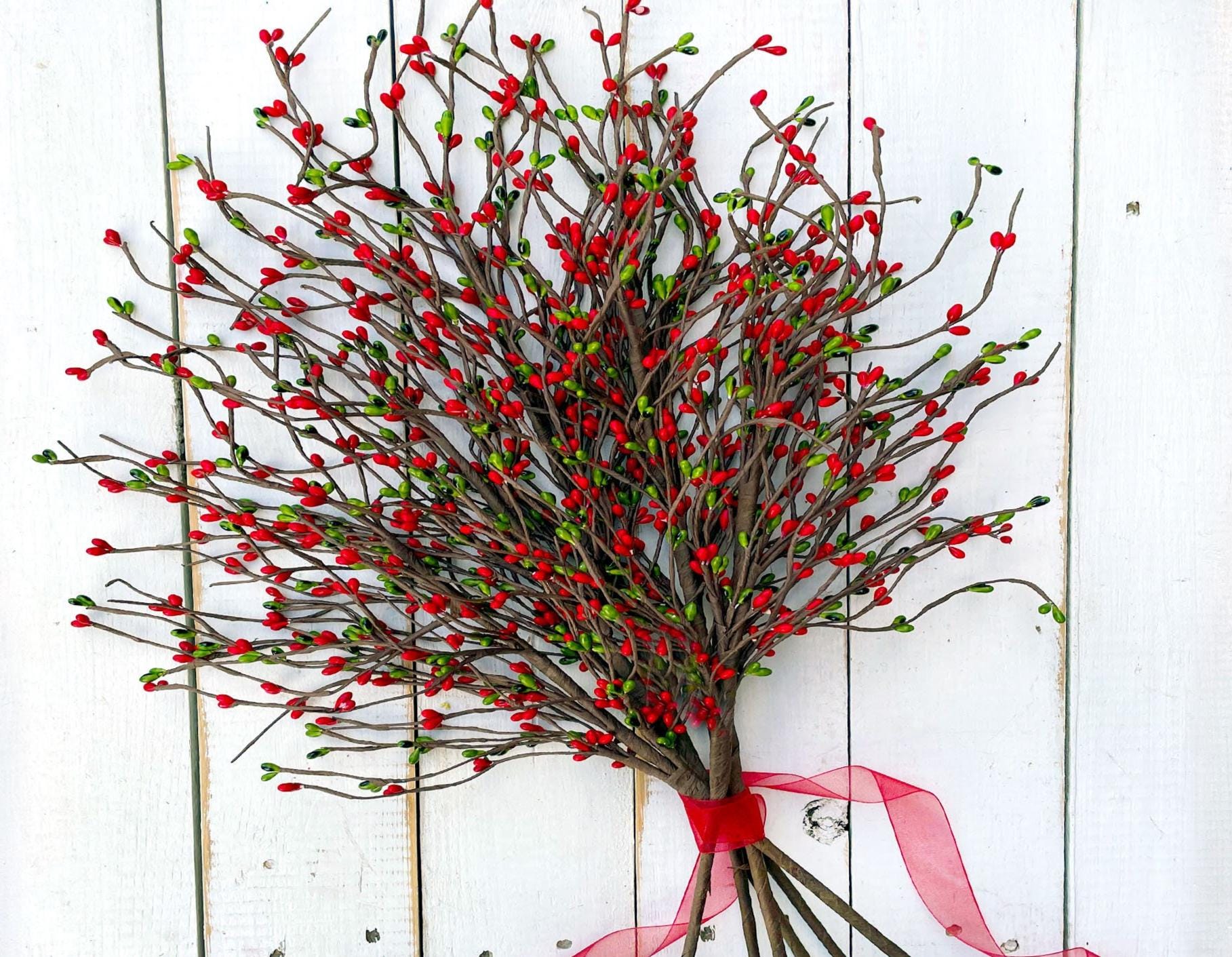 Decorative wreath with red berries and a pink ribbon on a white wooden background