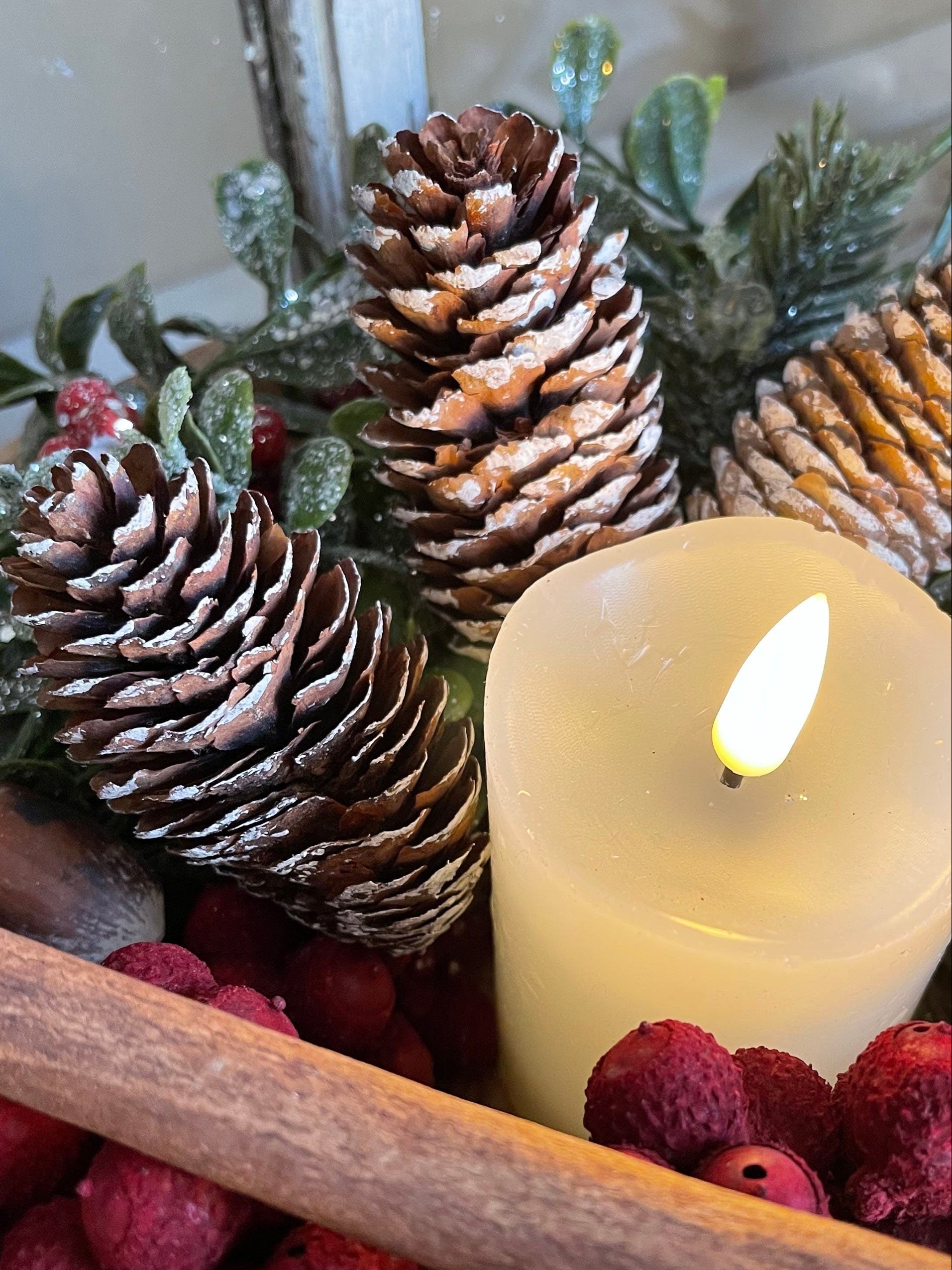 Decorative arrangement with pine cones, berries, and a candle on a white background.