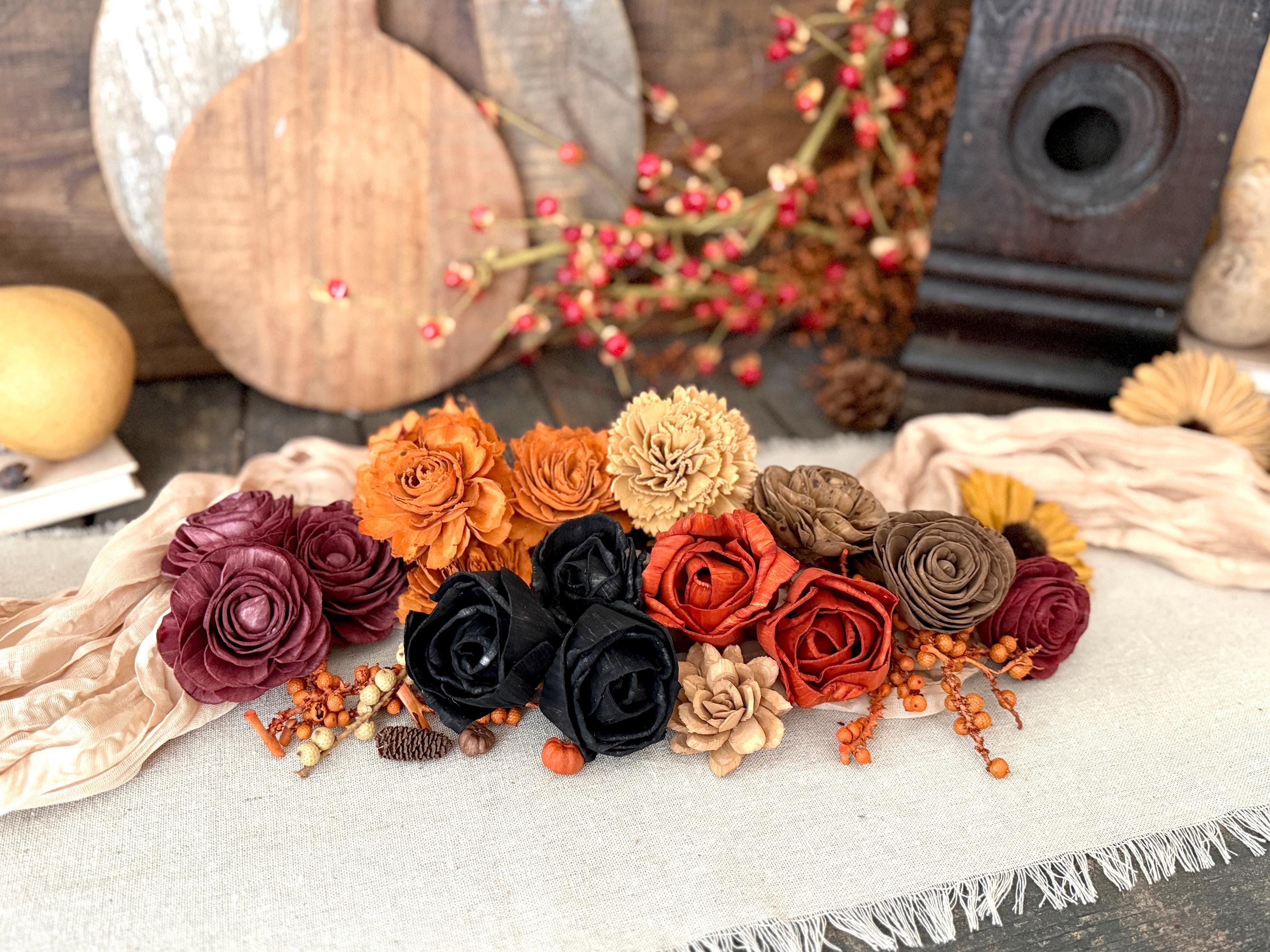 Decorative arrangement of autumn-themed wood flower blossoms on a textured surface with pumpkins and berries in the background.