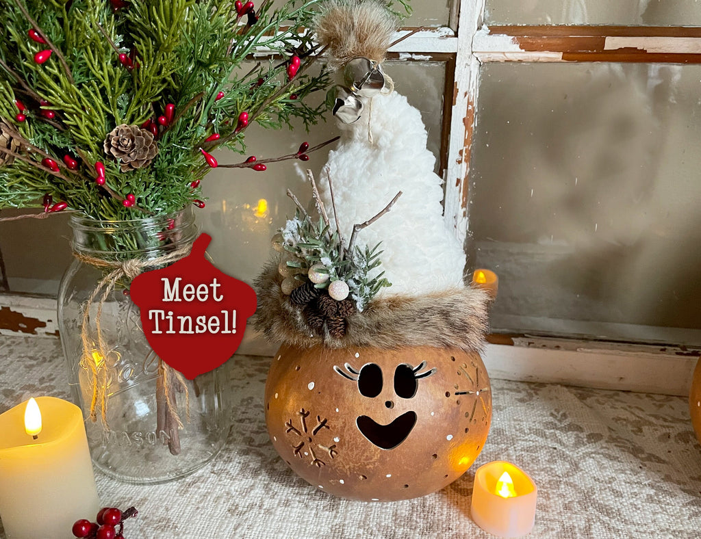 Decorative pumpkin with face, jar of greenery, and candles on a textured surface.