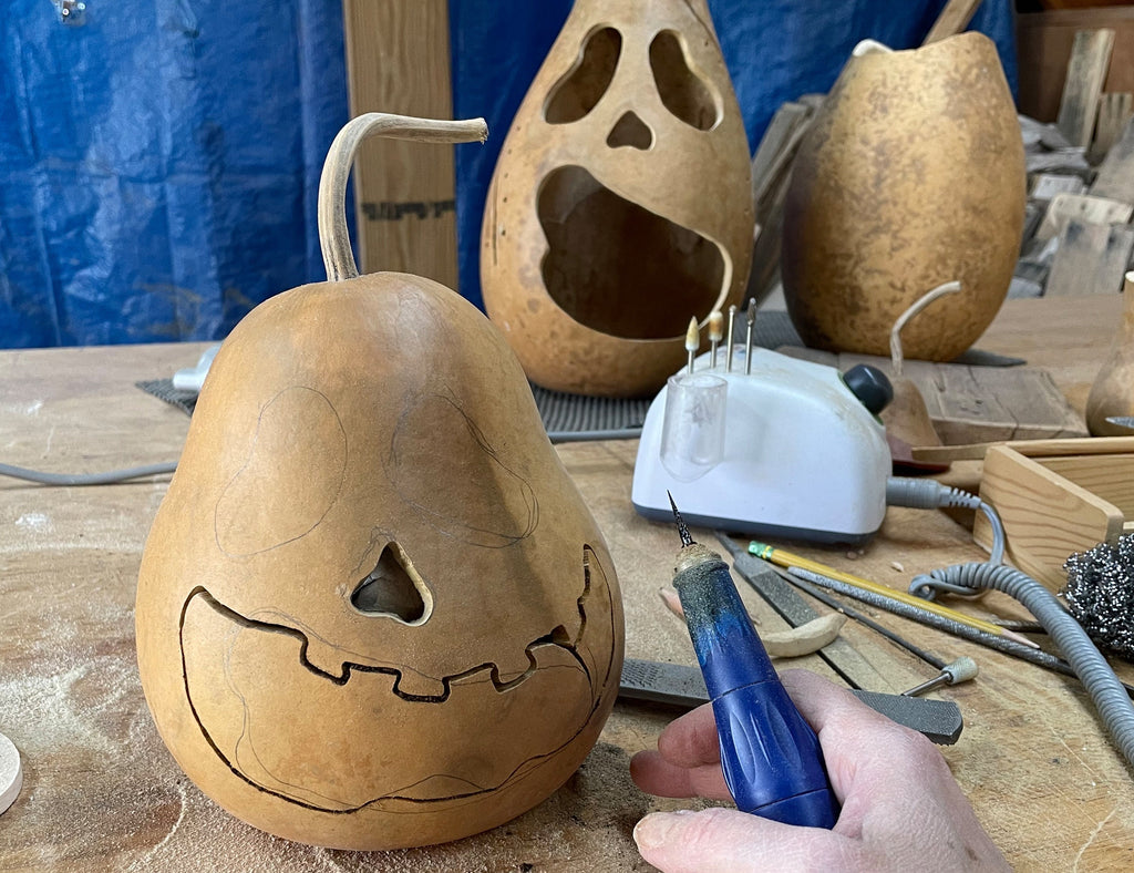 Carving a gourd with a face using a tool on a workbench.