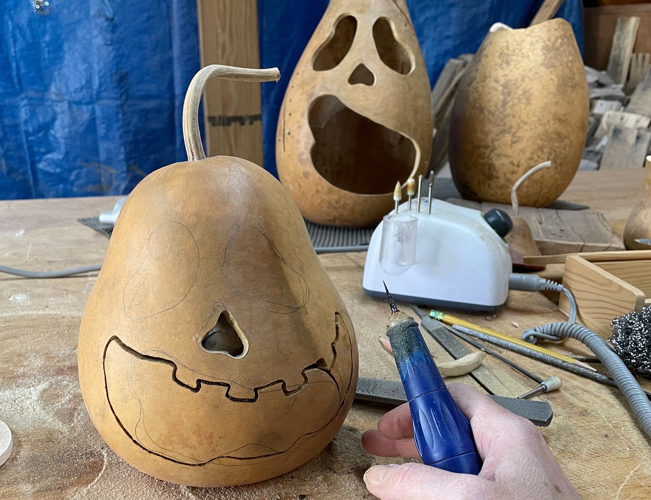 Carving a gourd with a face using a tool on a workbench.
