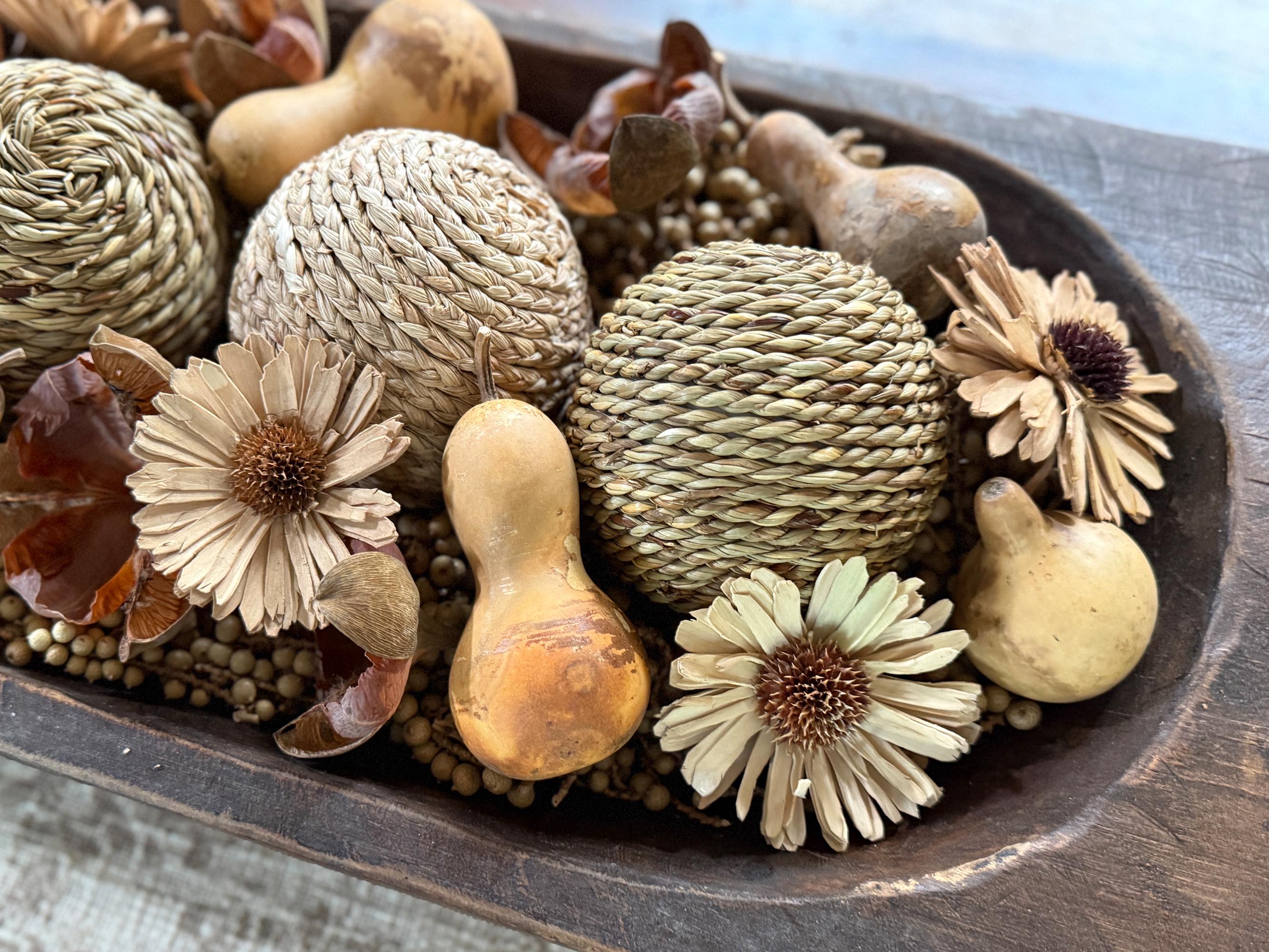 Decorative arrangement of gourds, seeds, and flowers in a wooden bowl.