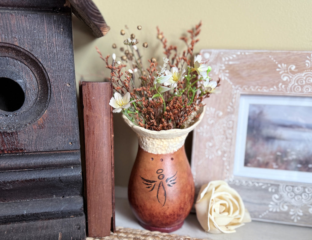 Decorative gourd vase with dried flowers next to a wooden birdhouse and a rose on a surface.