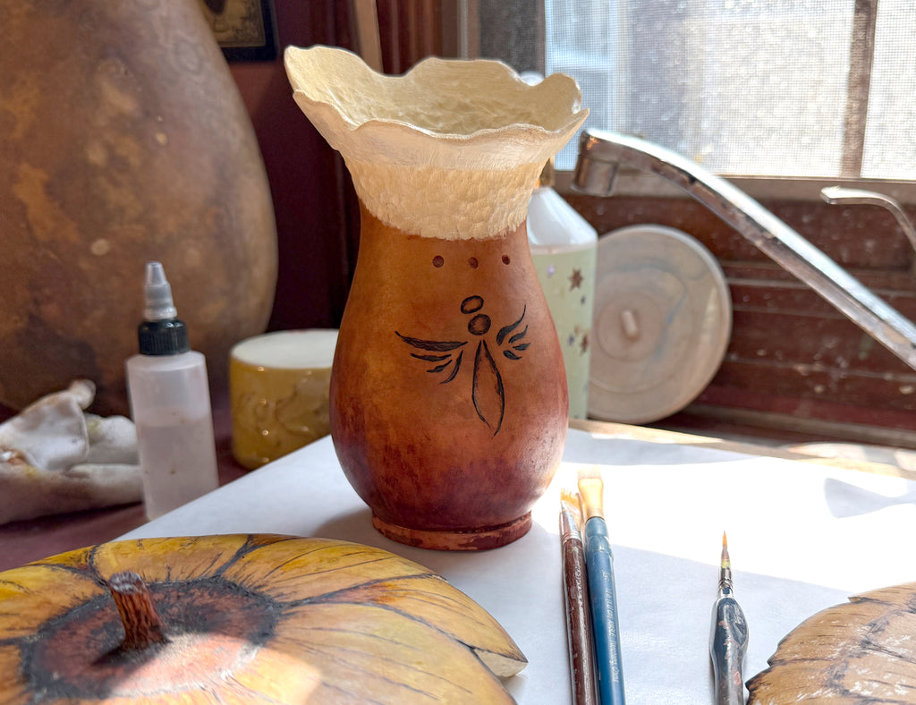 gourd vase with a decorative angel design on a table with art supplies