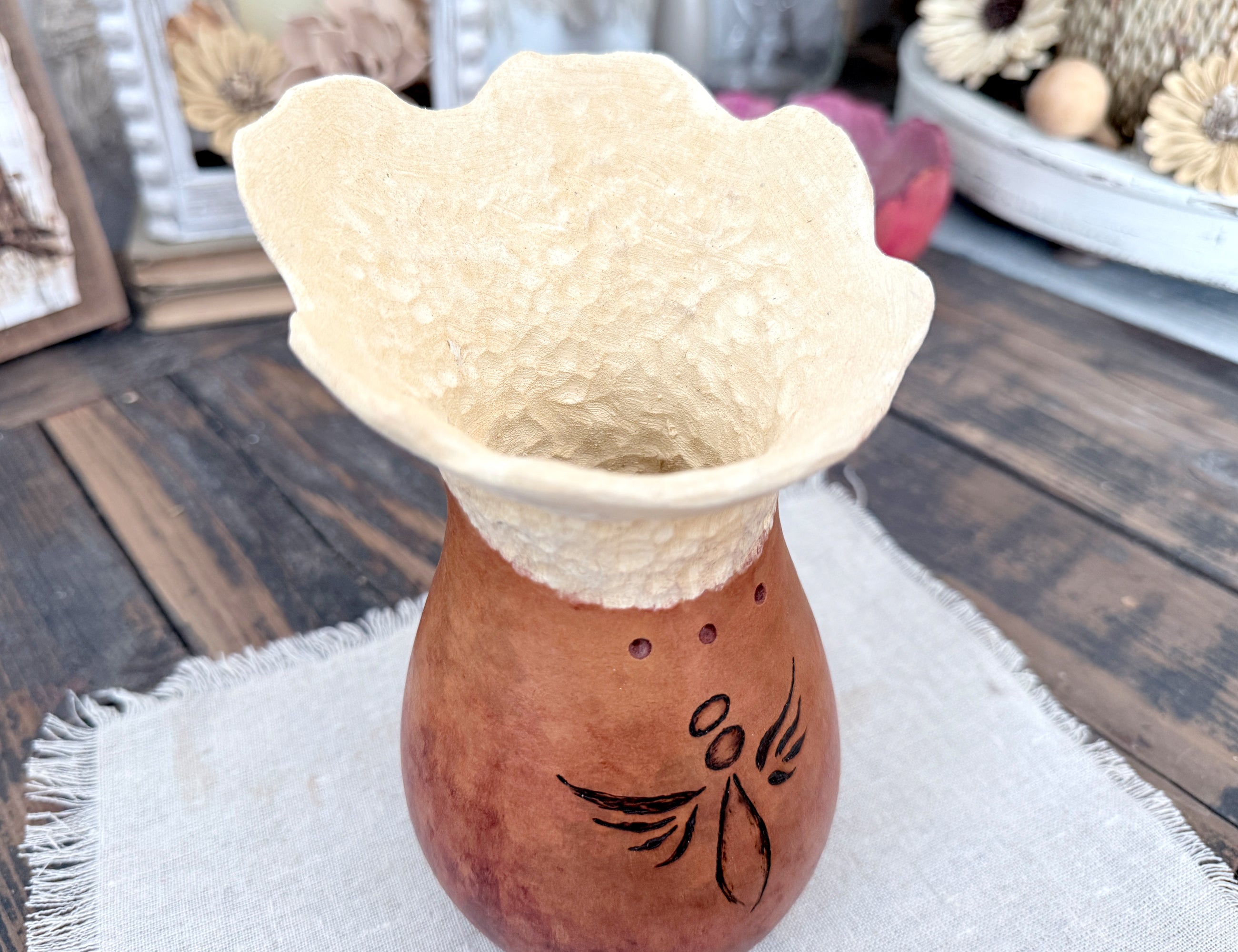 Ceramic vase with textured top and floral design on a wooden surface