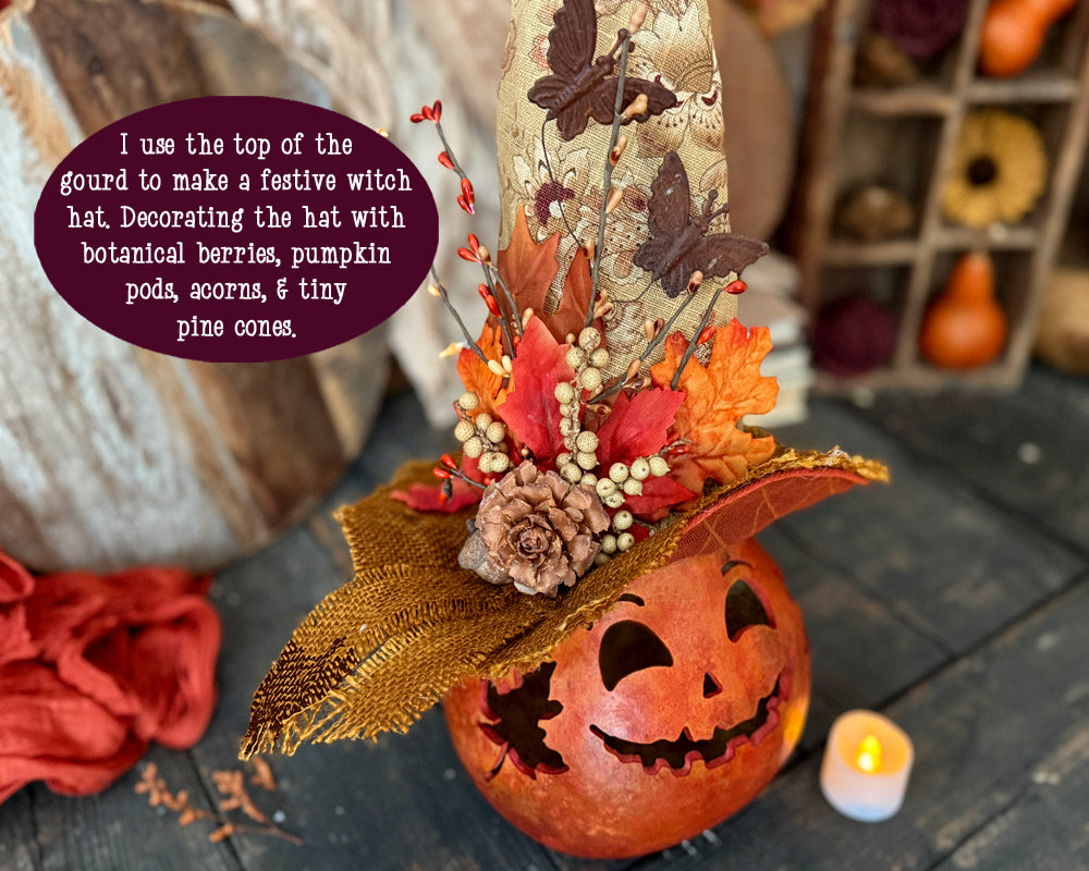 Decorative Halloween pumpkin with a witch hat made from gourd top, berries, and leaves on a wooden surface.