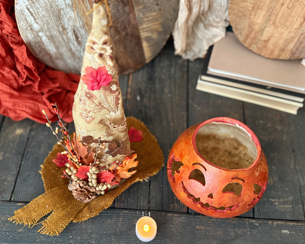 Decorative items including a cone with flowers, a pumpkin lantern, and a candle on a wooden surface.