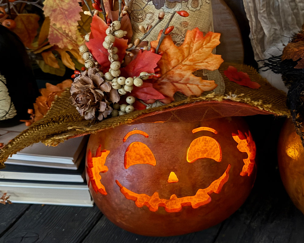 Decorative pumpkin with carved face and autumn leaves on a wooden surface