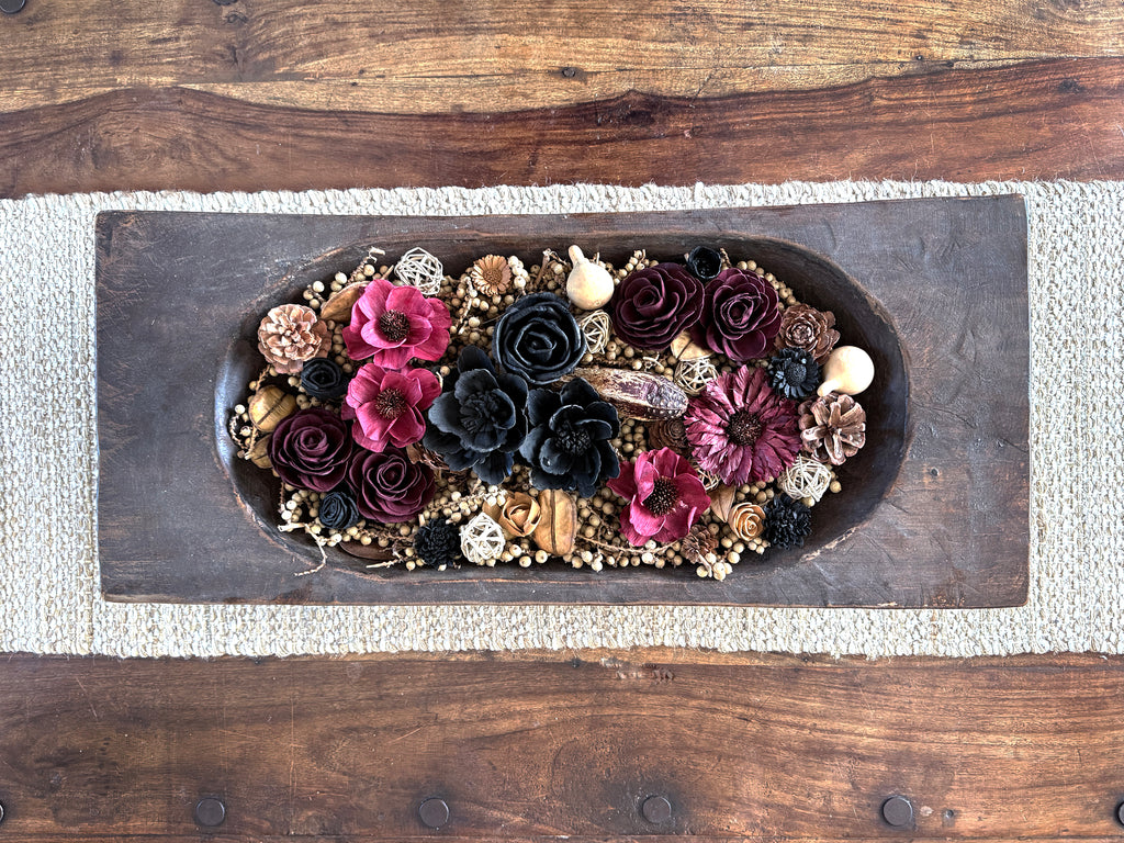 Decorative dough bowl arrangement of flowers and decorative elements on a coffee table.