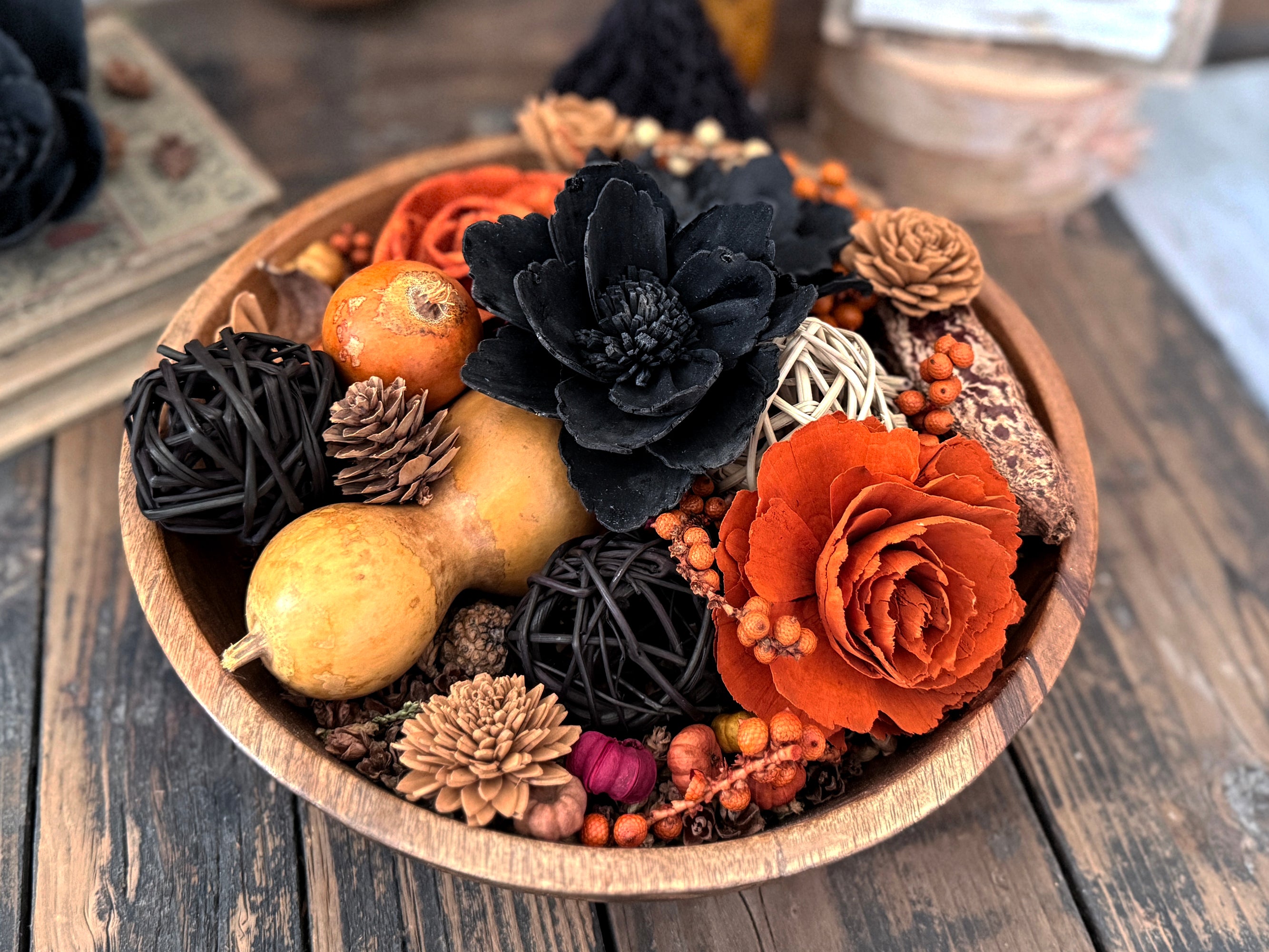 Decorative bowl with autumn-themed elements including flowers, gourds, and pinecones on a wooden surface.