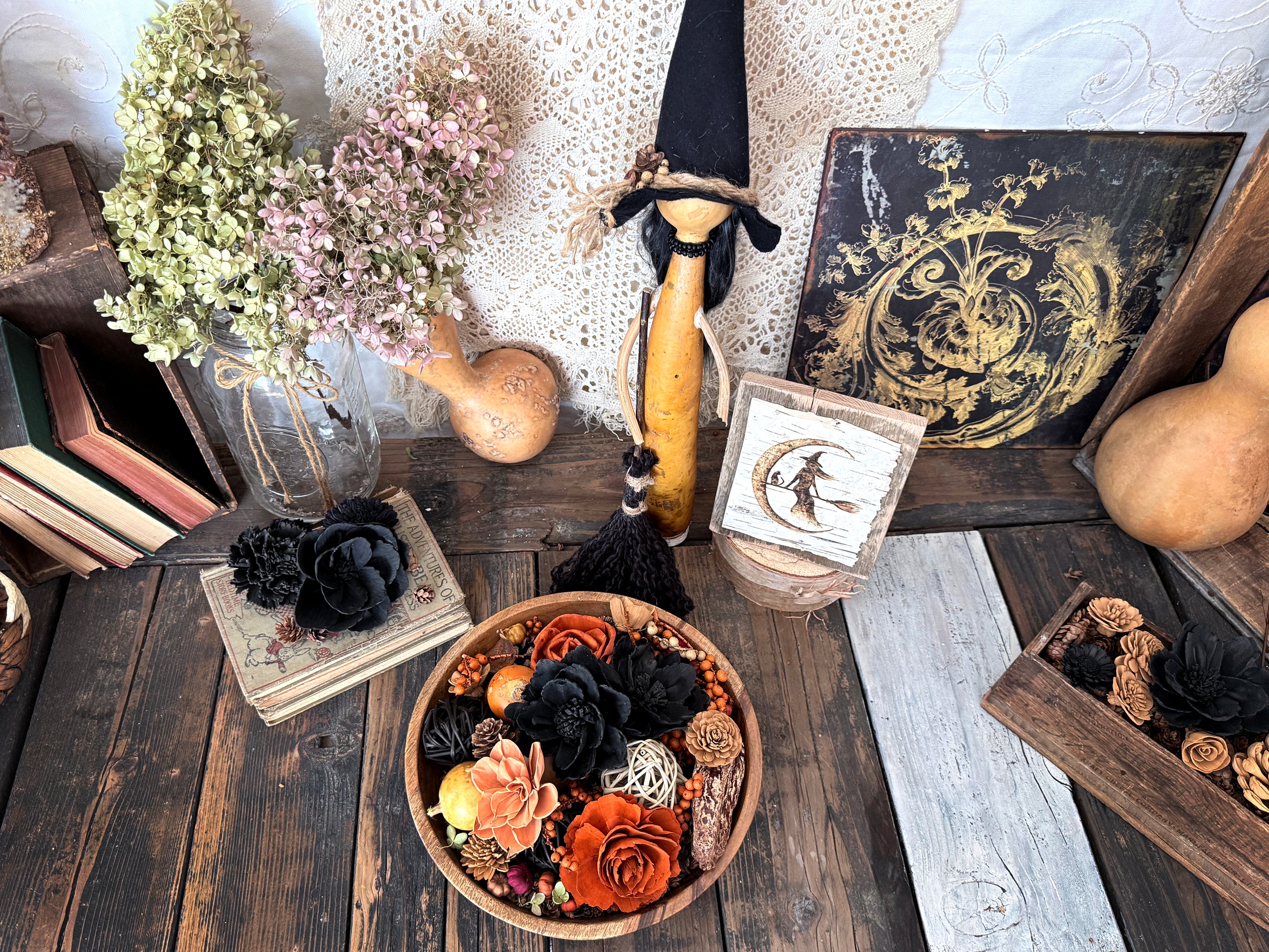Decorative setup with flowers, gourds, and a witch figure on a wooden surface.