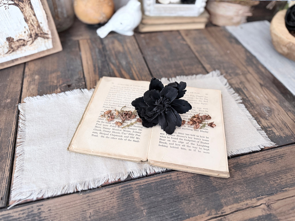 Open book with a black flower on a wooden surface