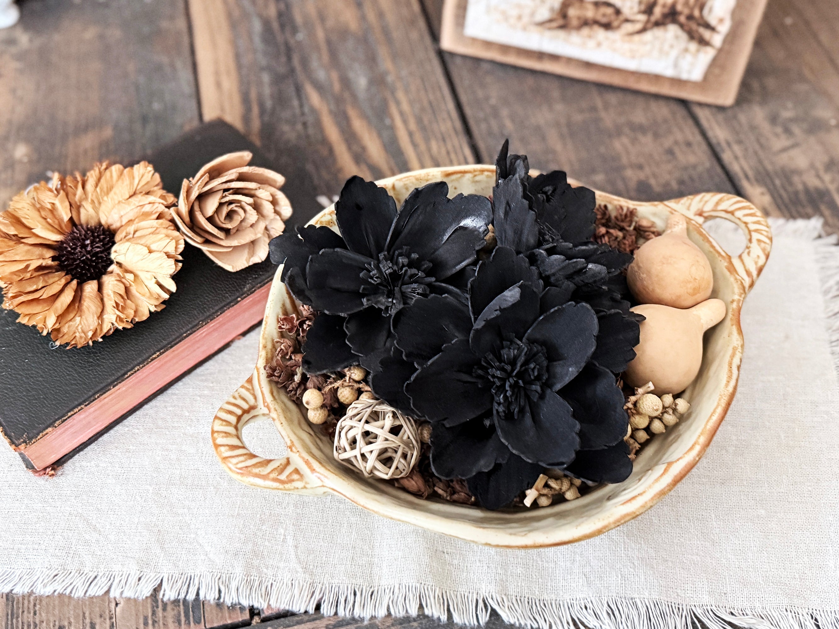 Decorative bowl with black flowers, beige roses, and spherical objects on a wooden surface.
