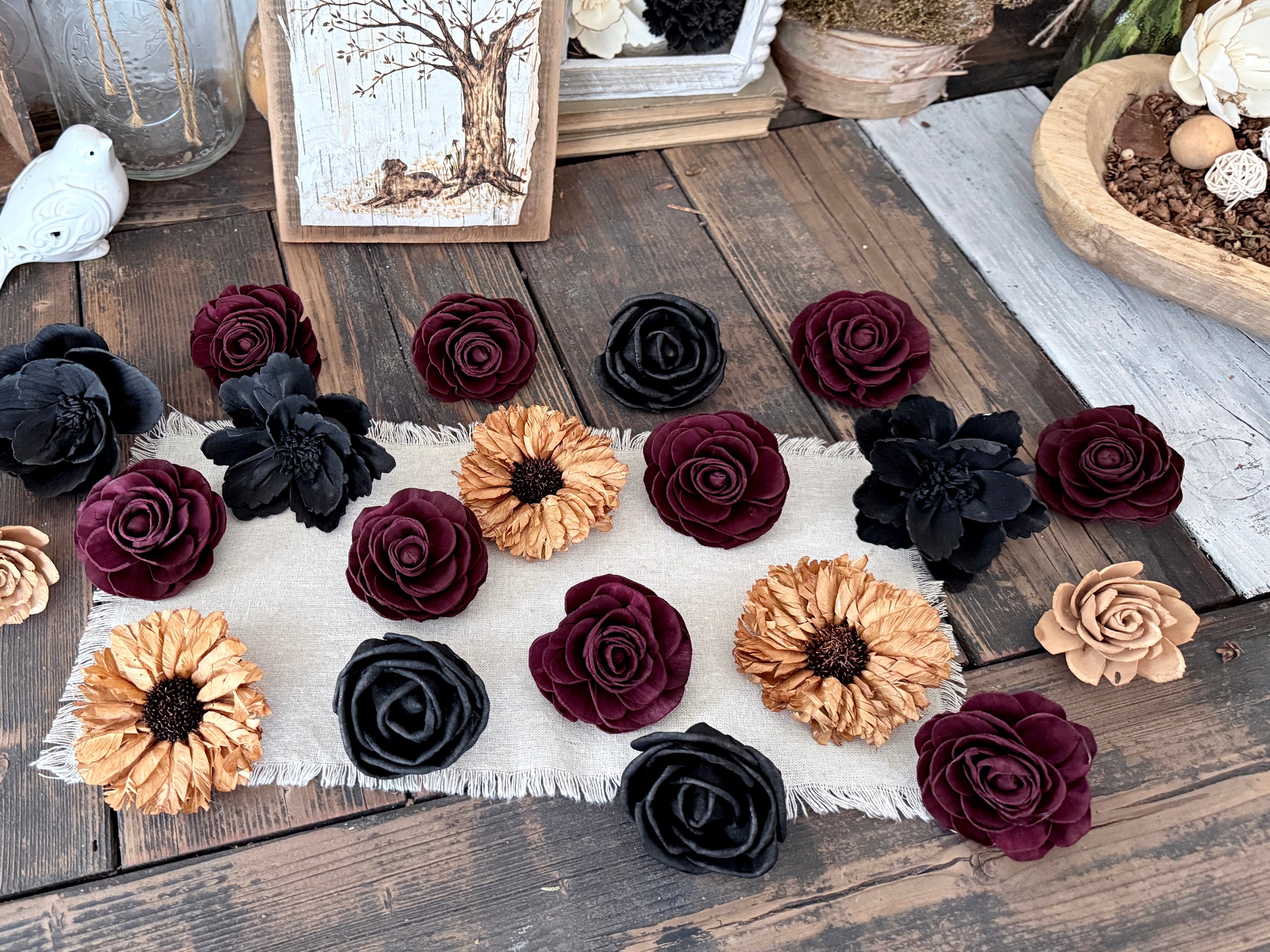 Assorted wood flowers on a wooden surface with a white cloth underneath. Flowers are in gold, black and burgundy.