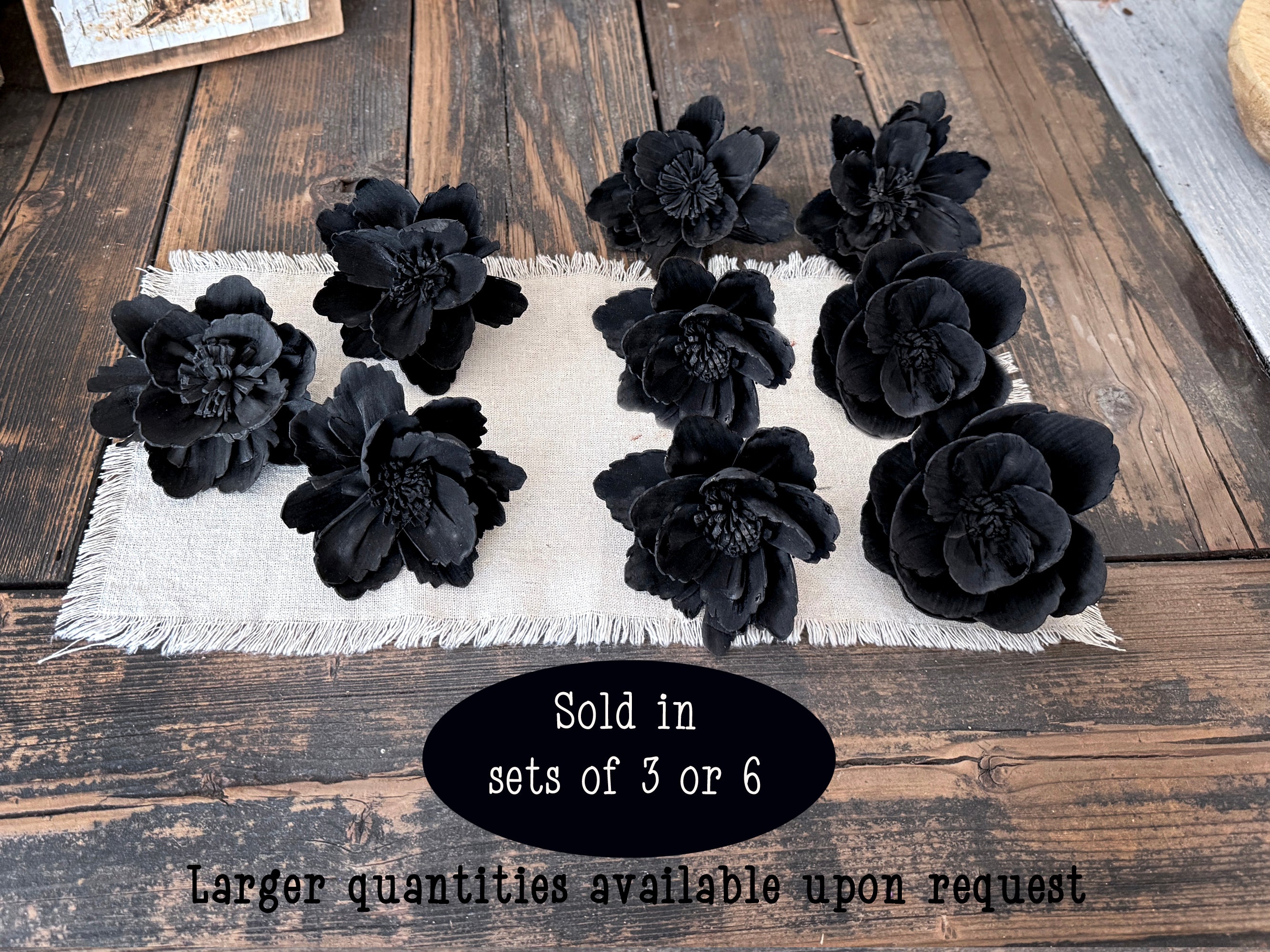 Black floral decorations on a white linen with text about quantity availability on a wooden surface.