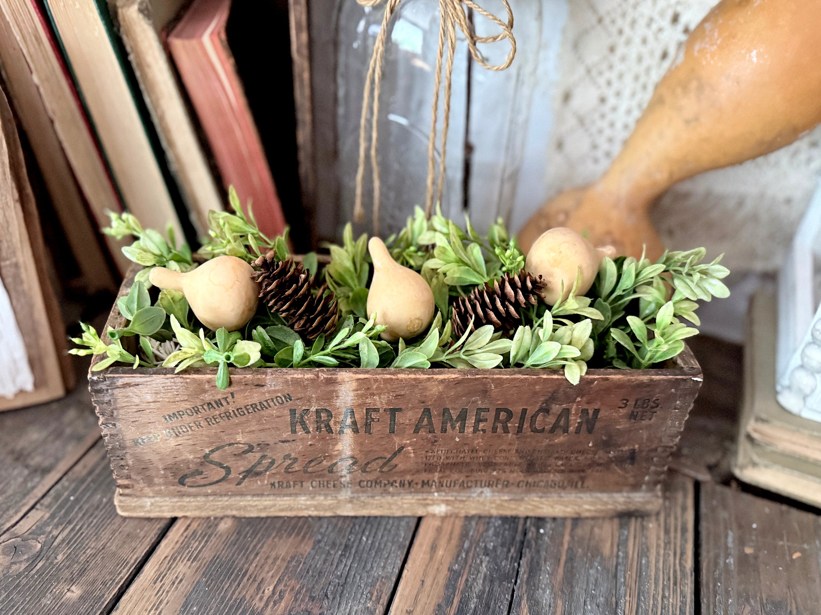 Vintage cheese box holding a boxwood greenery arrangement with pine cones and gourds 