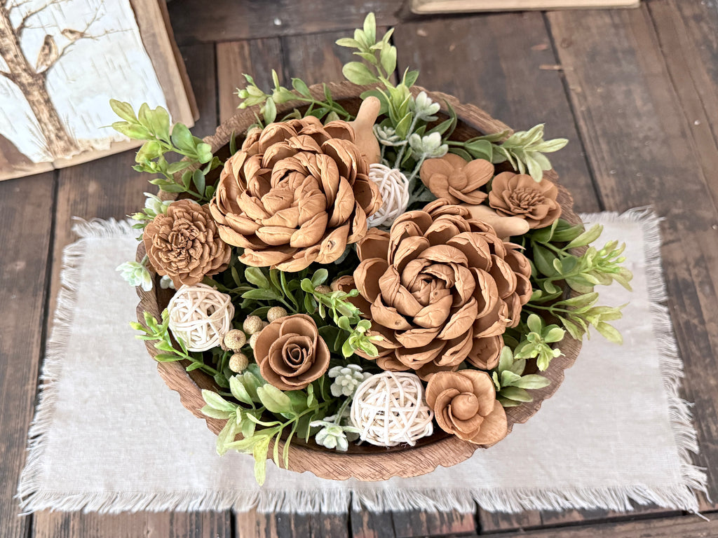 Decorative teak wood bowl with brown and white wood flowers on a wooden surface